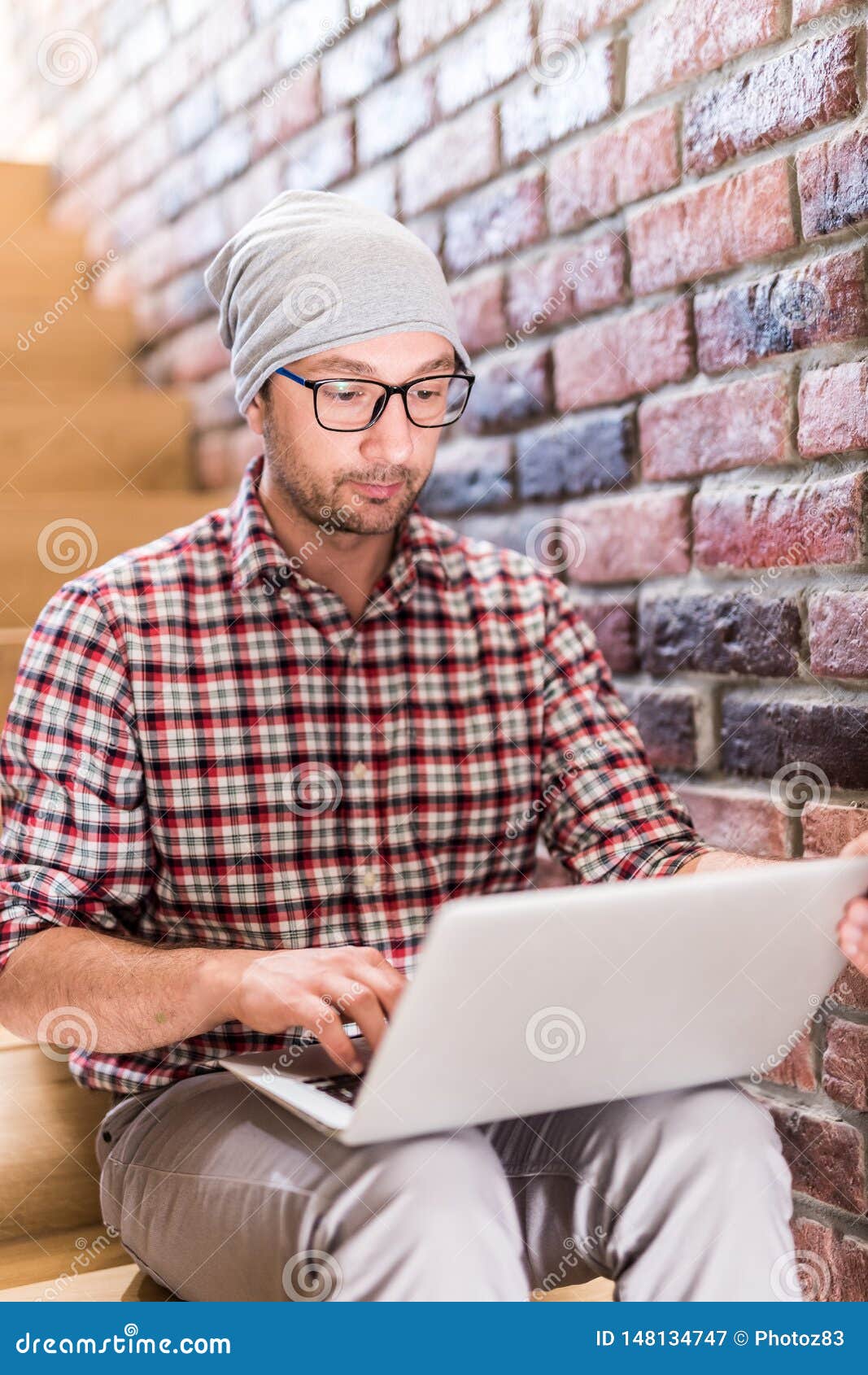 Portrait of modern hipster sitting on stairs and working on his laptop. Ung trendig blogger som arbetar p