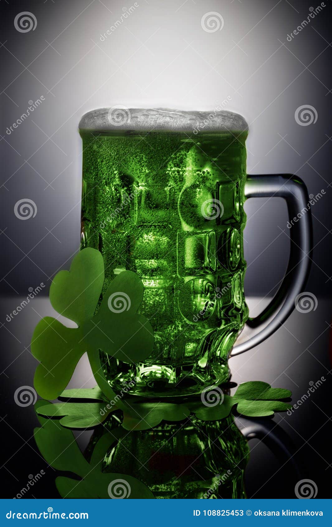 St. Patrick Day concept. Shiny glass of green beer on black background with shamrock.