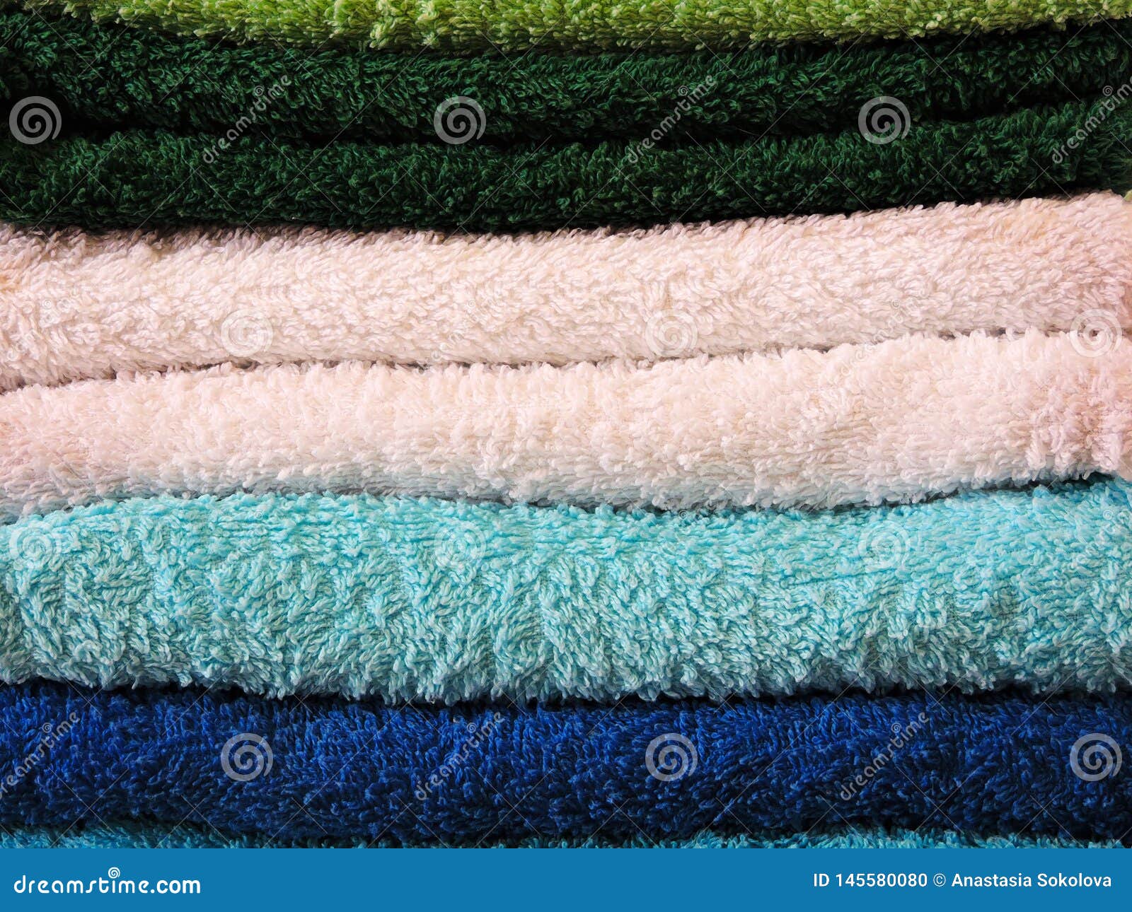 stack of bath towels on light wooden background closeup.pile of rainbow colored towels.top view.
