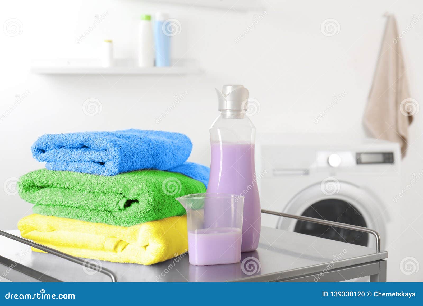 Stack of Clean Towels and Detergent on Table in Laundry Room. Stock