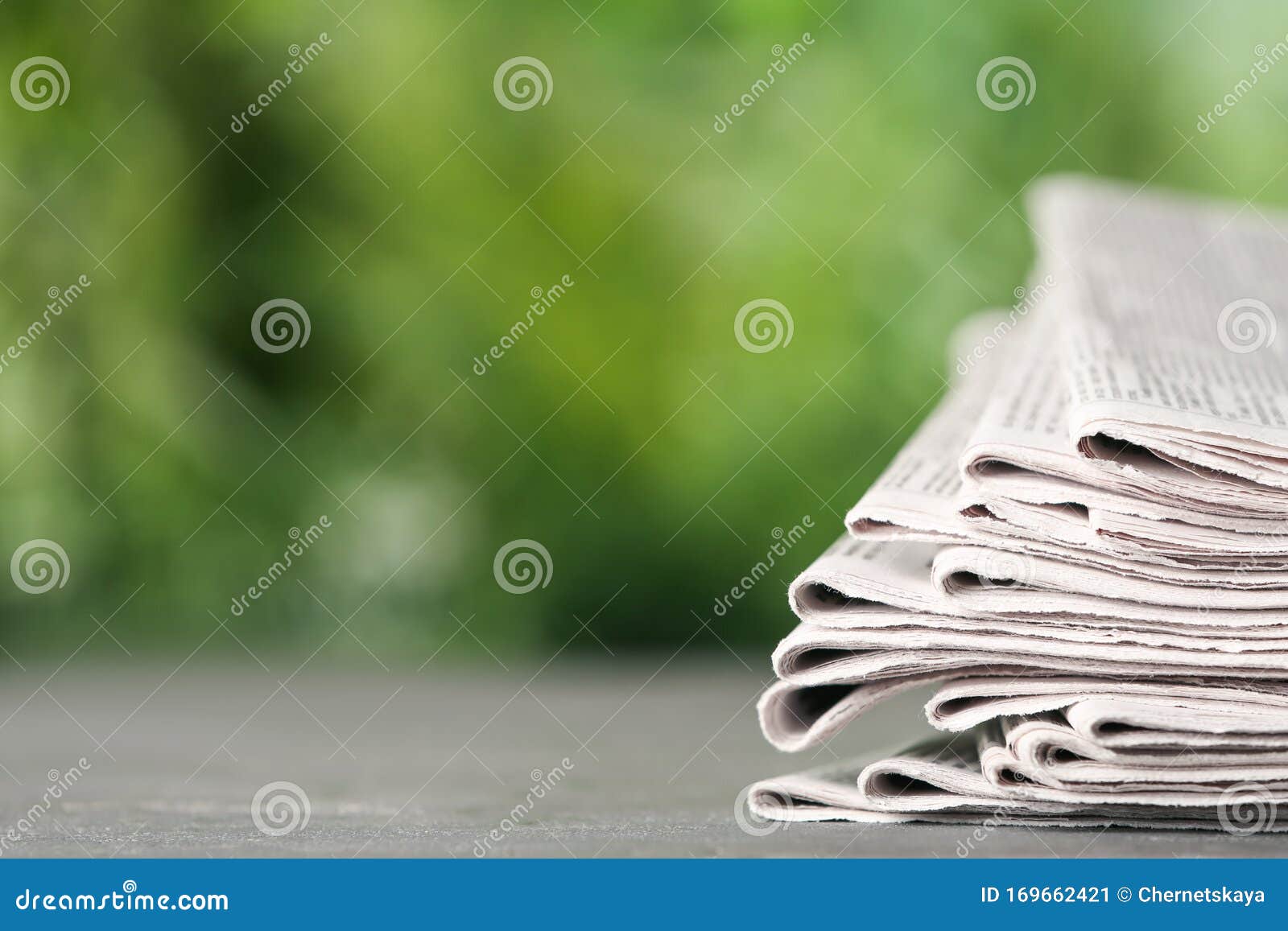 Stack of Newspapers on Grey Table Against Blurred Green Background