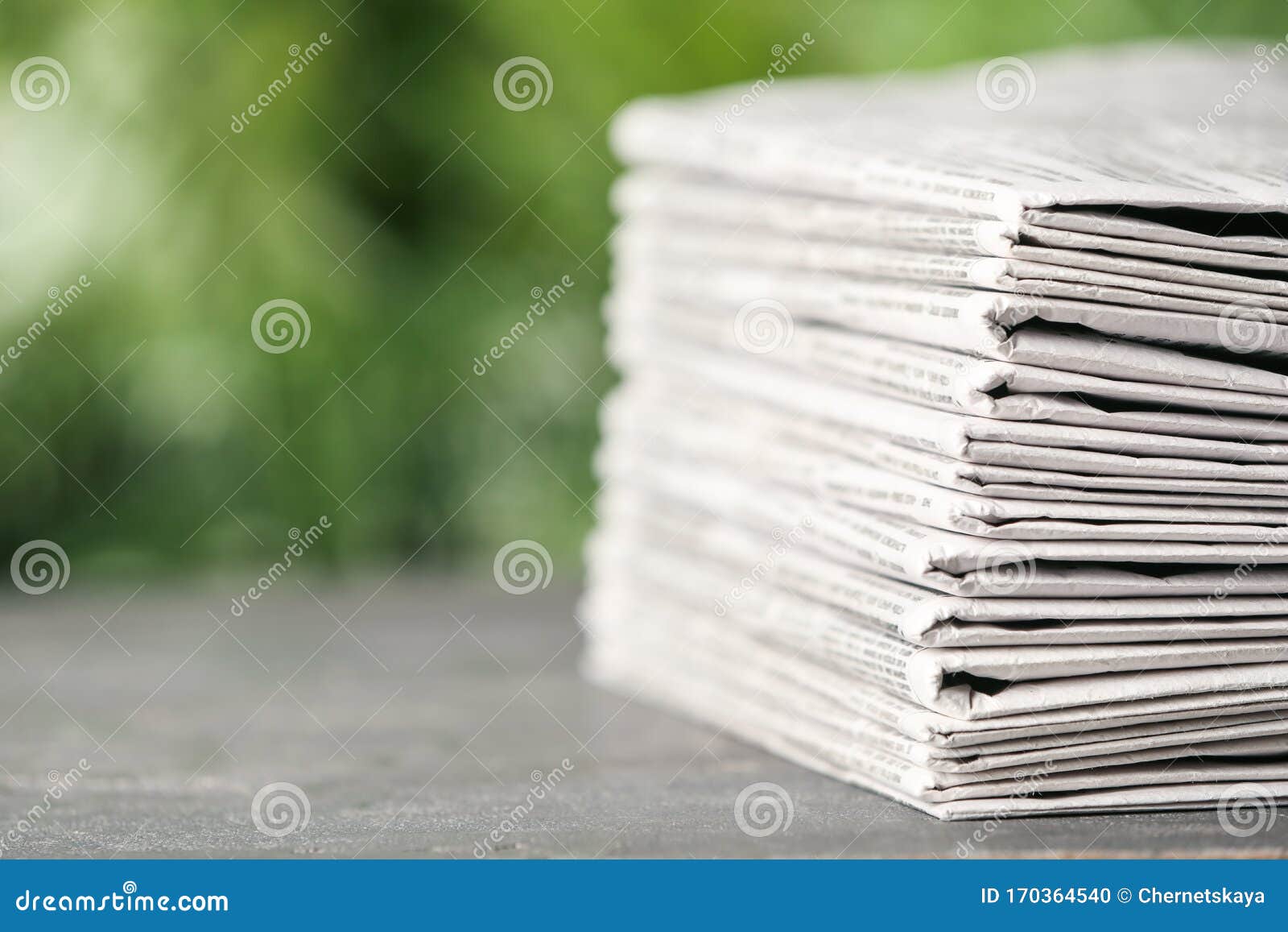 Stack of Newspapers on Grey Table Against Blurred Green Background