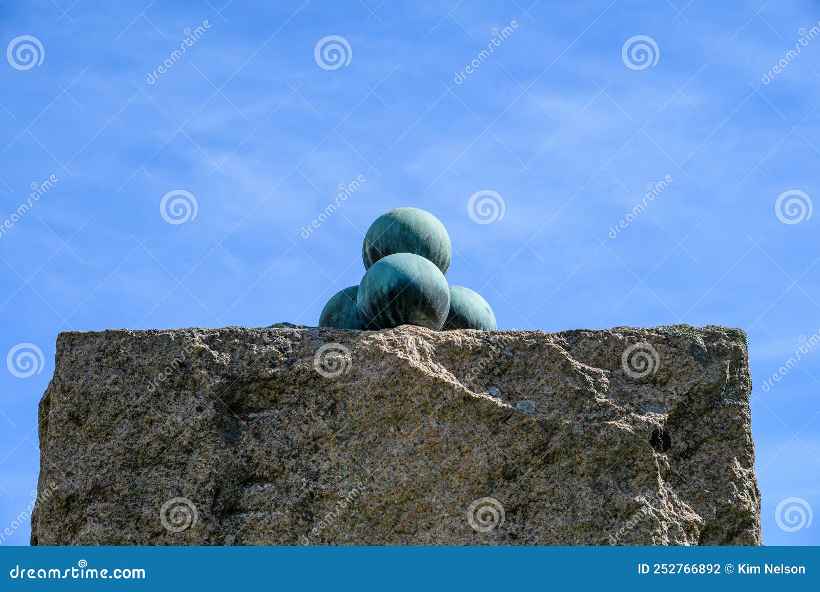 stack of old oxidized cannon balls on top of a rock pillar against a sunny blue sky, oscarsborg fortress, historic ww2 site in nor