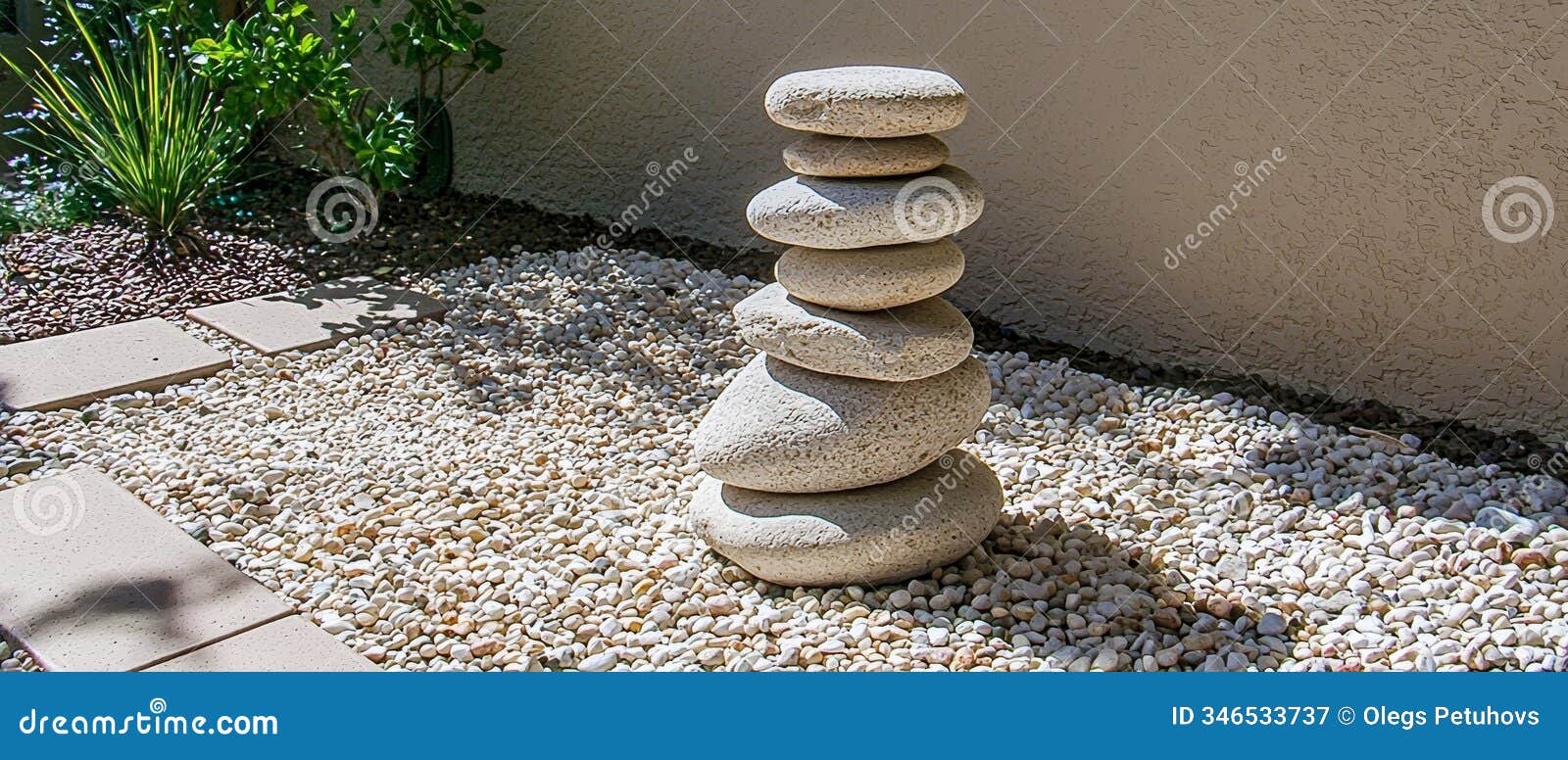 a stack of rocks in the graveled area, near a wall and a potted plant