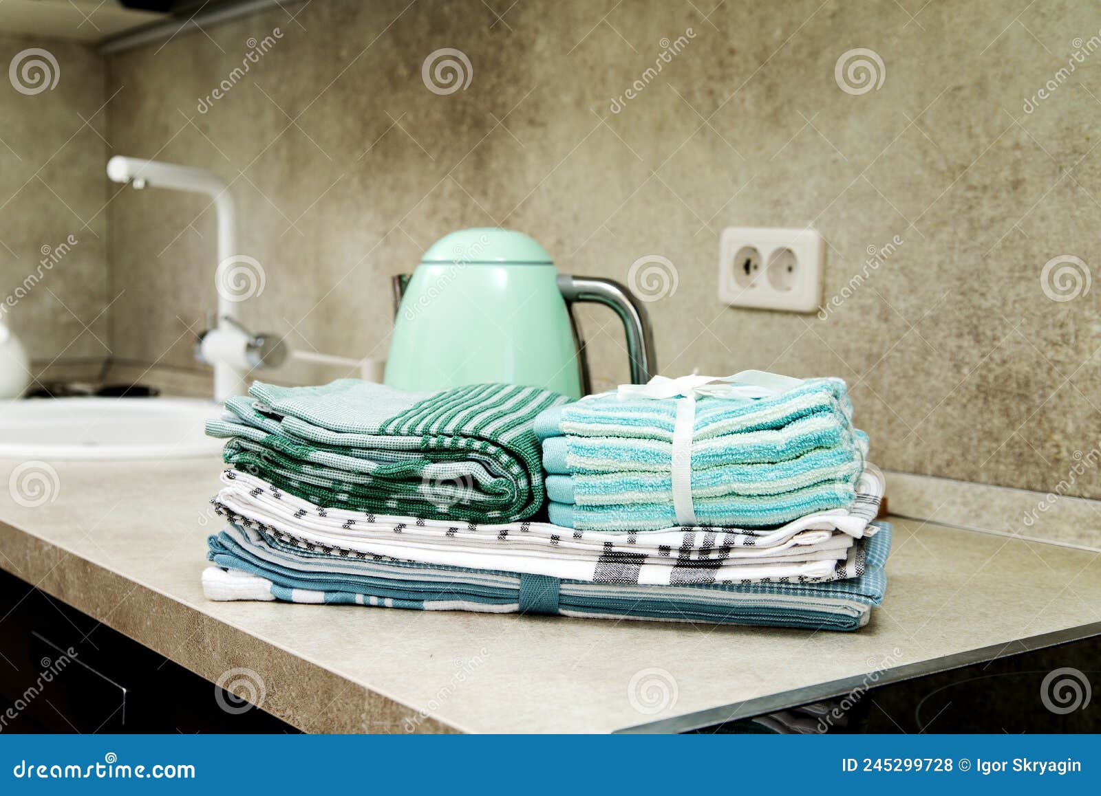 Stack of Various Kitchen Towels and a Turquoise Electric Kettle in a Bright Kitchen with a Sink