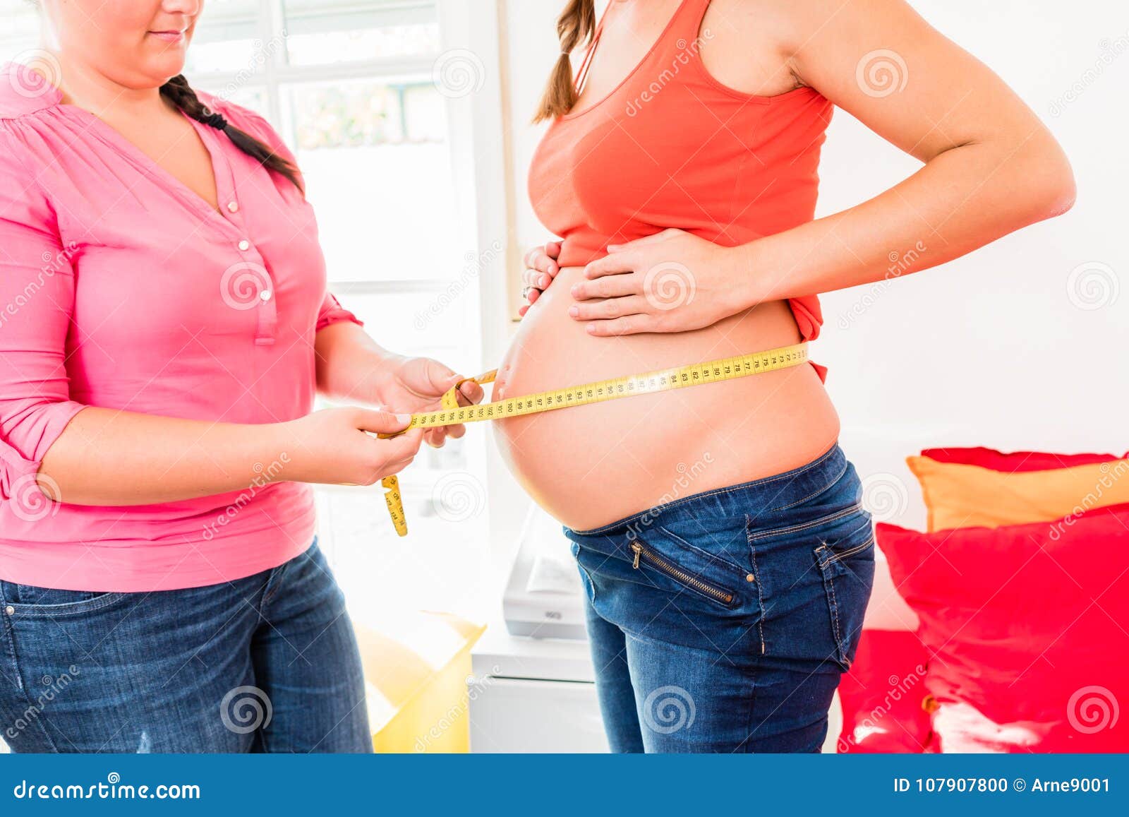 standing pregnant women and midwife measuring circumference of b