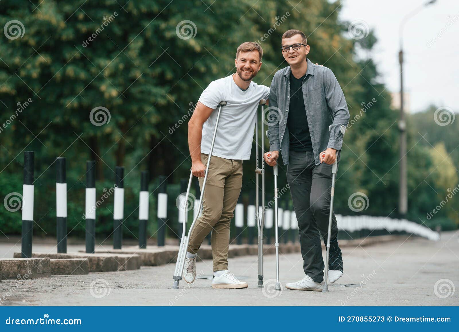 Standing and Smiling. Two Men with Crutches is Outdoors on the Road