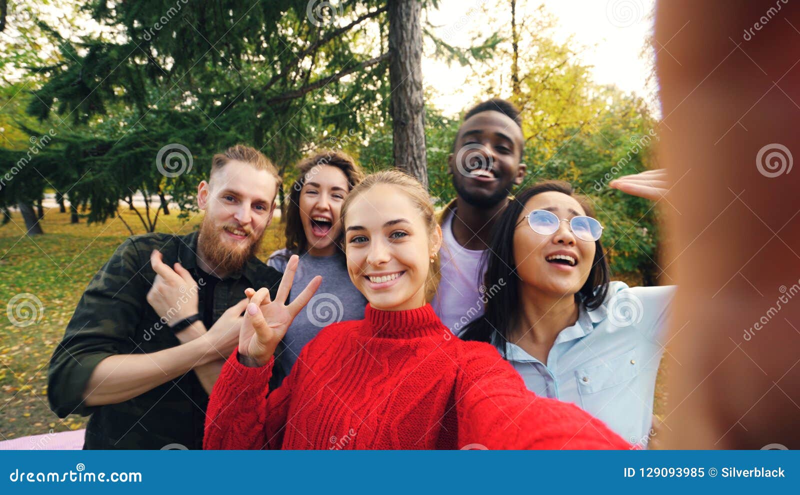 Standpunt van het jonge apparaat van de vrouwenholding met camera en het nemen selfie met vrienden multi-etnische groep wordt ges. Standpunt van jonge vrouwen wordt geschoten die apparaat met camera houden en selfie met vrienden multi-etnische groep nemen in park in de herfst die Fotografie, vrije tijd en mensenconcept