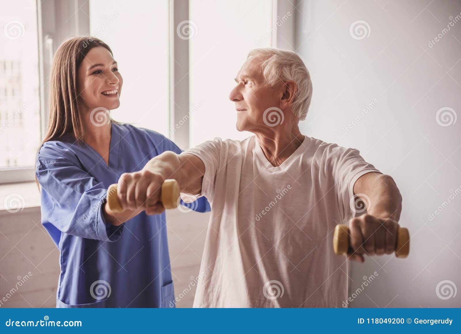 Stary szpitalny mężczyzna. Przystojni starzy człowiecy robią ćwiczeniom z dumbbells i one uśmiechają się, w szpitalnym oddziale Atrakcyjna pielęgniarka pomaga on