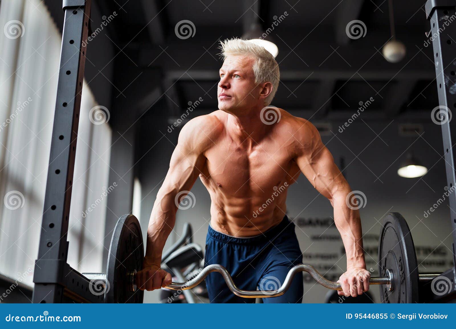 Sterke mens met het spierlichaam uitwerken in gymnastiek Gewichtsoefening met barbell in geschiktheidsclub