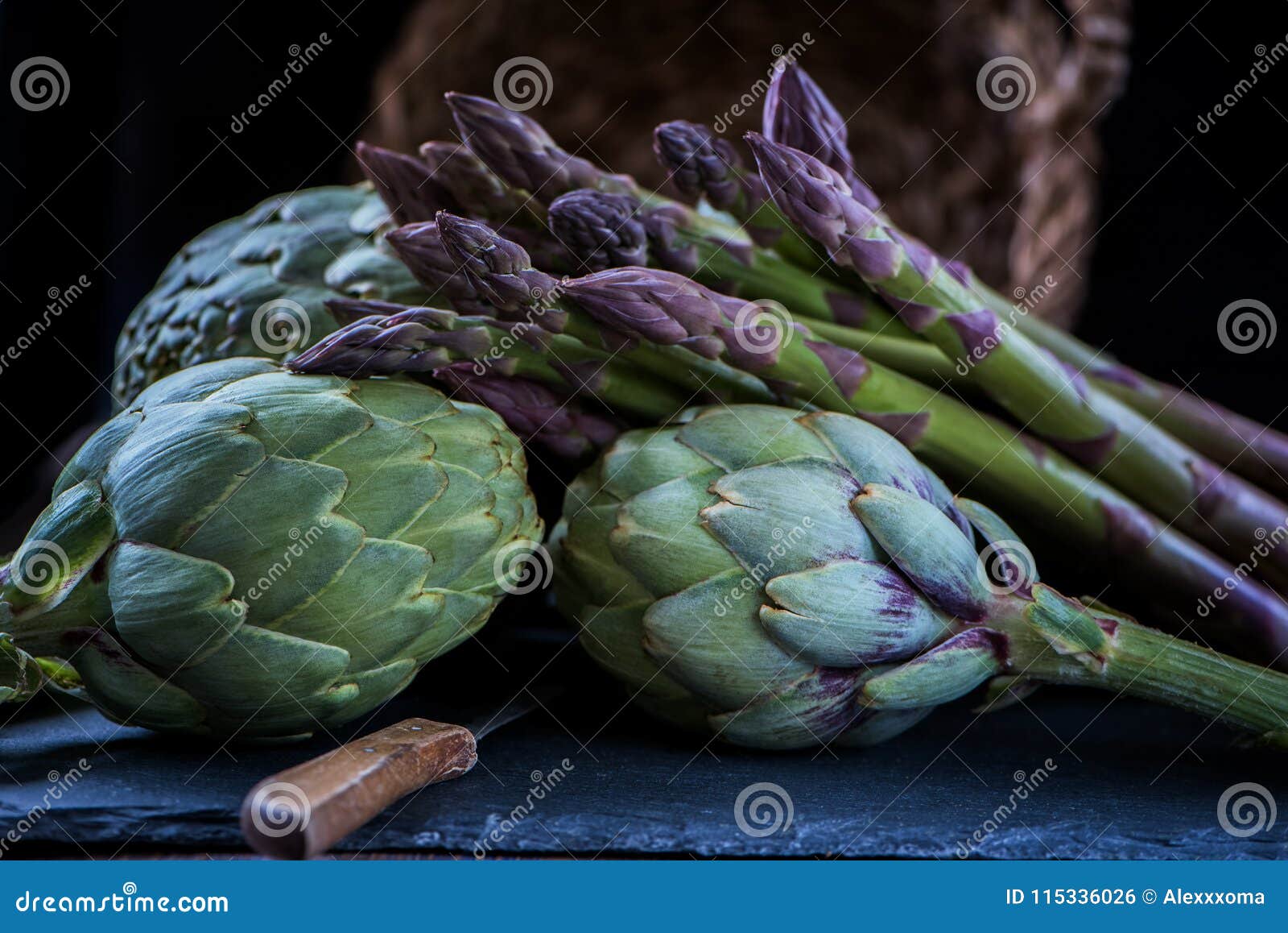 a still life of artichokes with knife and asparagus on the rustic textured background close side view low key