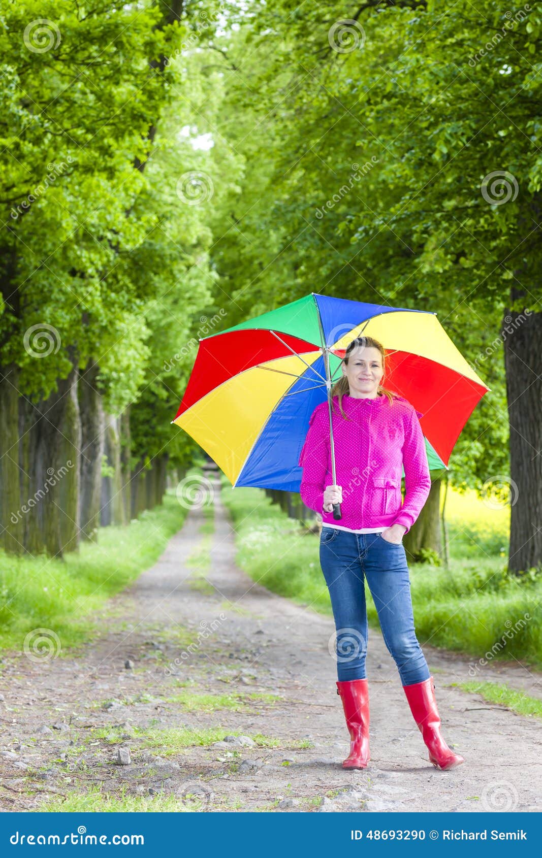 Stivali di gomma d'uso della donna con l'ombrello. Woman wearing rubber boots with umbrella in spring alley