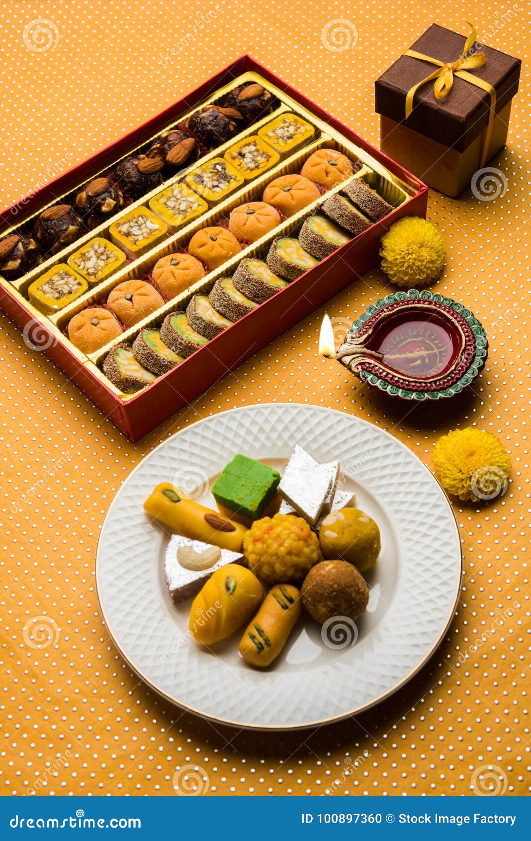 Indian sweets or Mithai for diwali festival with oil lamp or diya and gift box. Stock photo of Indian sweet or mithai and oil lamp or diya with gift box and flowers on decorative or colourful background, selective focus