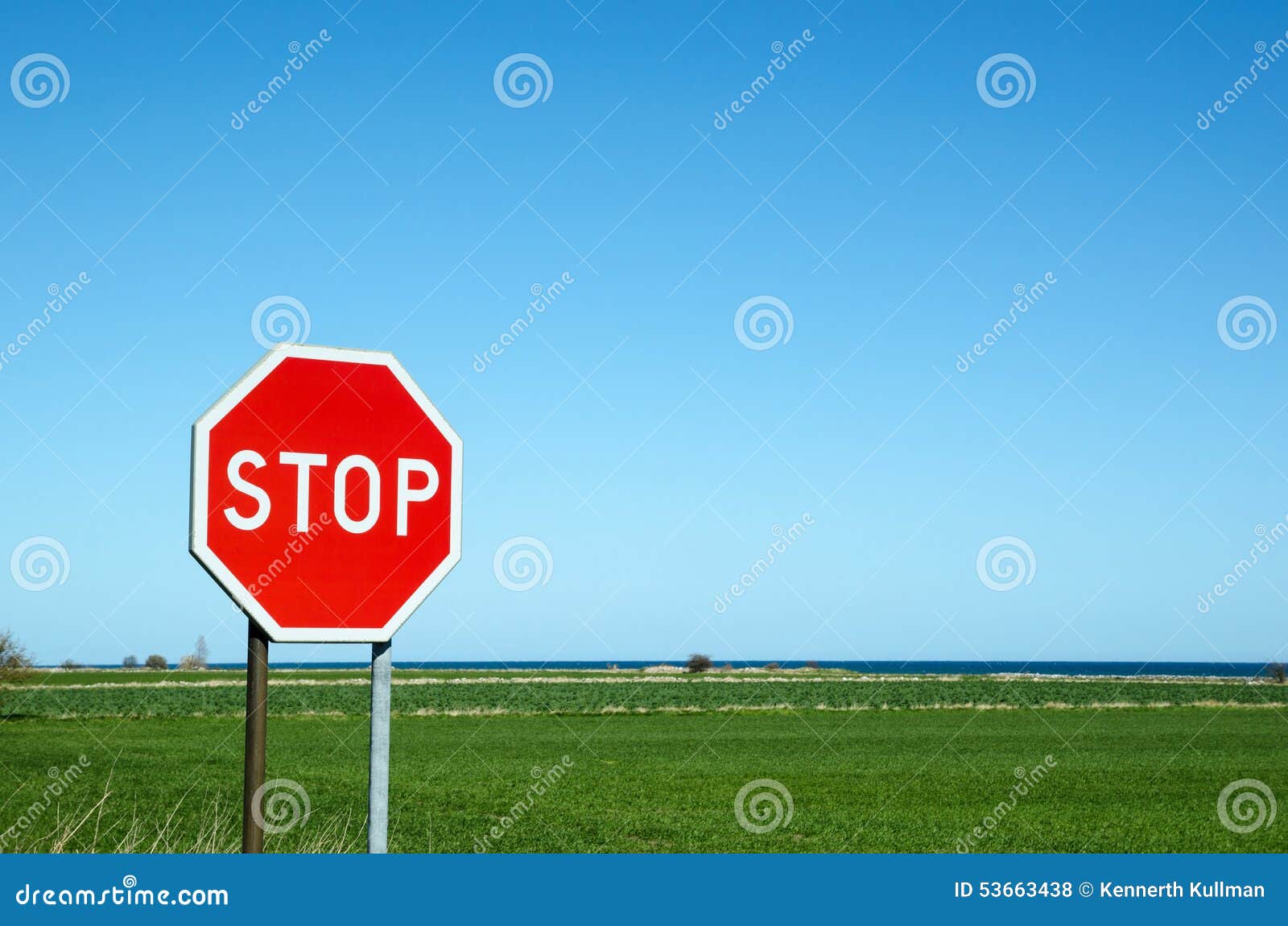 Stoppen Sie roadsign durch ein grünes Feld mit blauem Wasser im Horizont