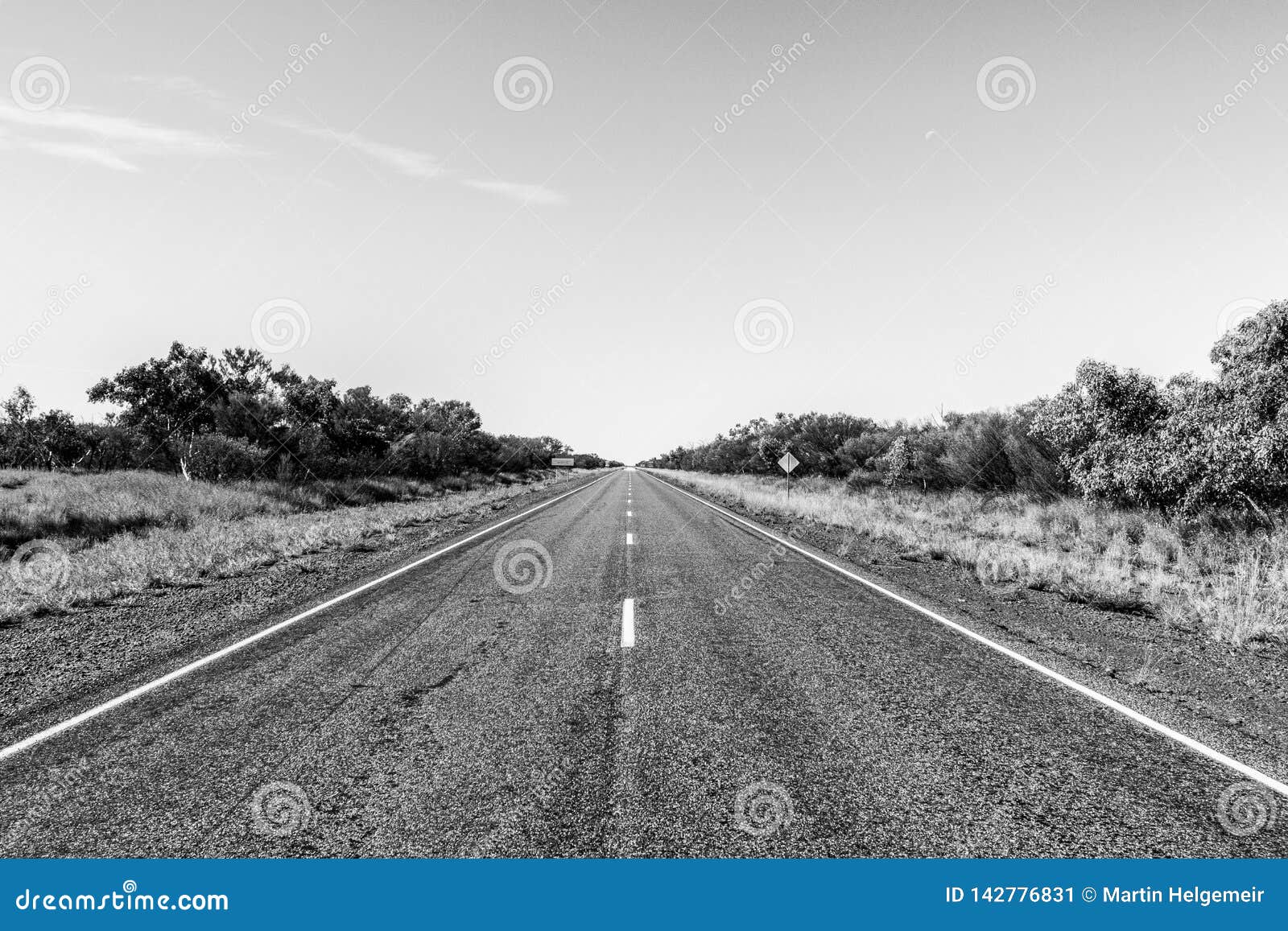 Strada diritta attraverso il dessert dell'Australia, Australia Meridionale, Stuart Highway Australia. L'immagine in bianco e nero del nullarbor, l'entroterra, natura vuota del paesaggio dell'azionamento di centro di viaggio della via della strada principale dell'Australia Stuart dell'estate di bellezza di sud del trasporto del downunder di orizzonte del Queensland del cespuglio del bitume diritto blu aperto soleggiato solo senza fine piano a distanza di colore chiaramente sbiadisce barriera verde delle gamme asciutte lunghe della steppa della strada la bella per esplorare le nuvole di festa dell'asfalto del tramonto dell'infinito di avventura di distanza di azionamento