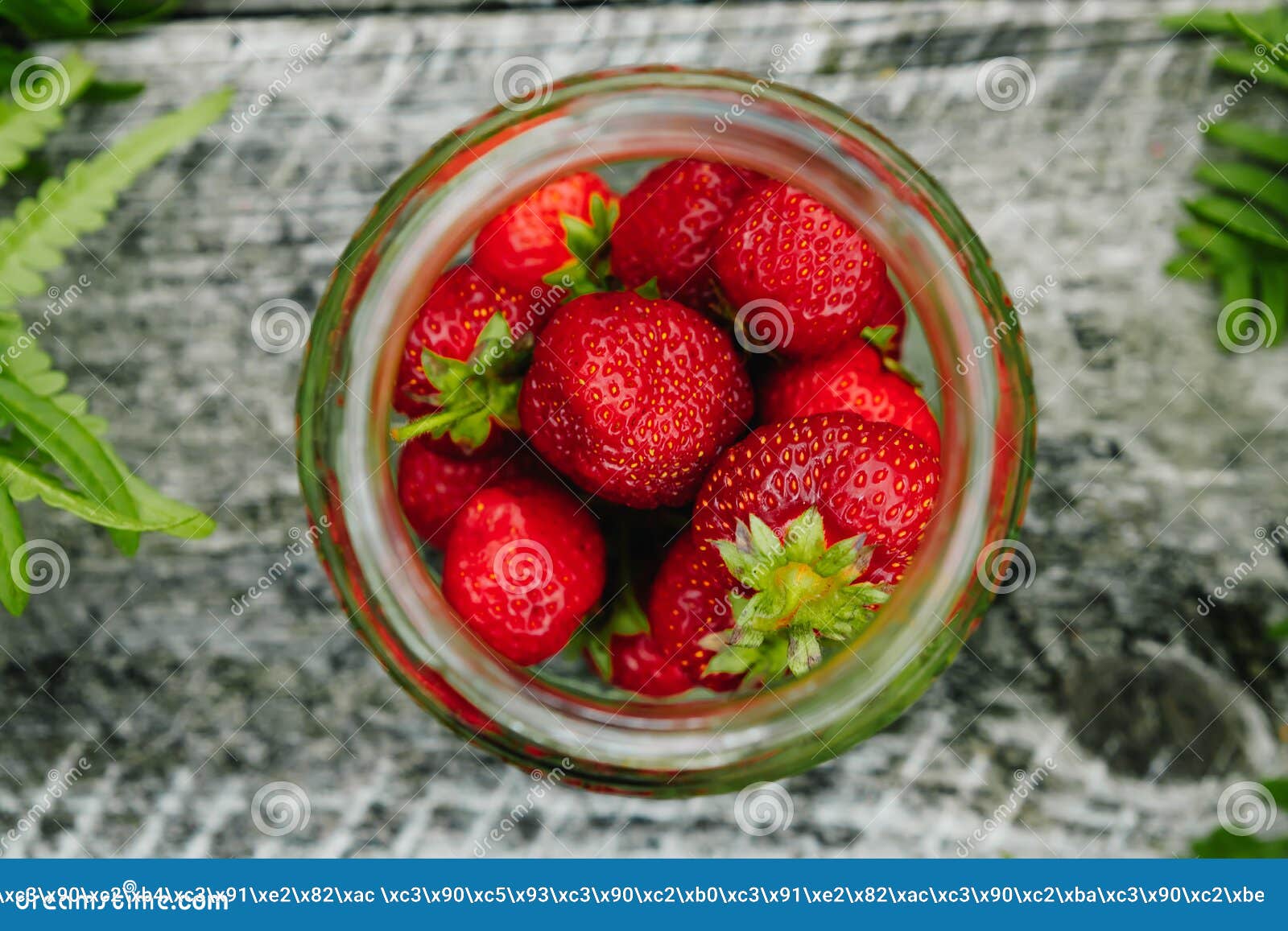 strawberries in a glass jar on a wooden gray table on a green background, leaves of paparatnik, strawberry season