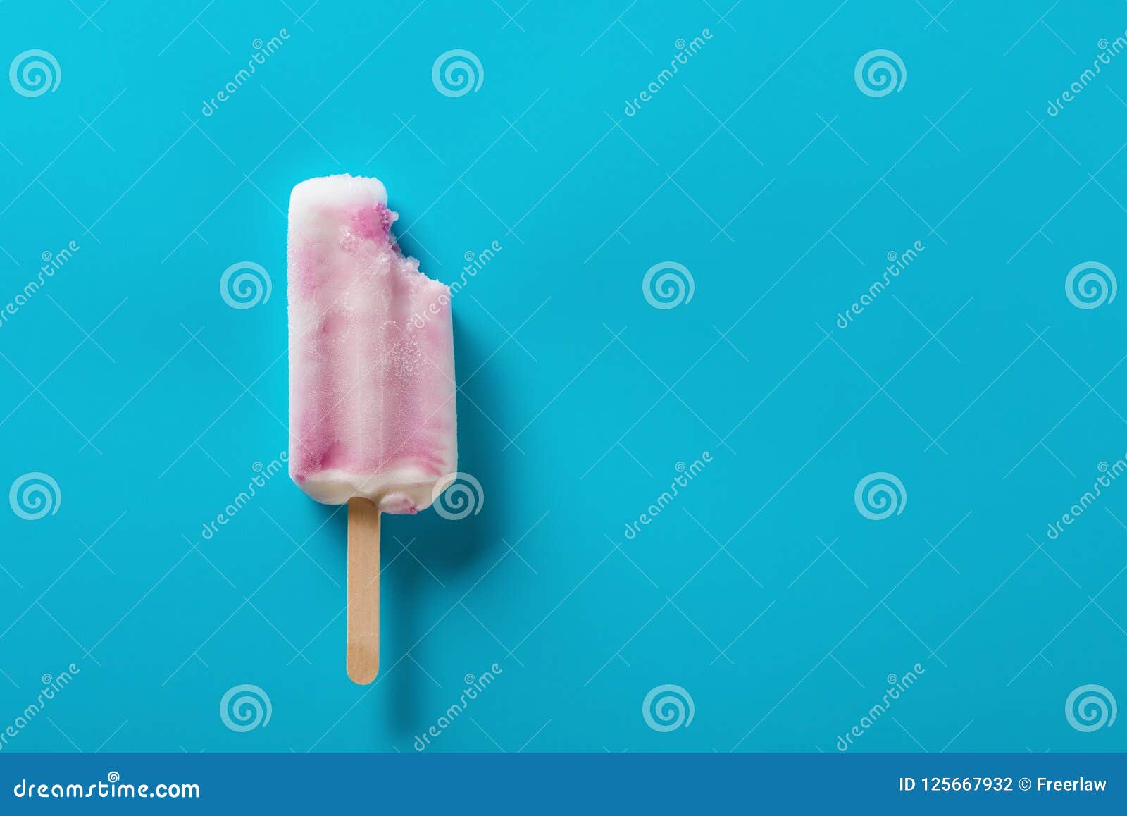 Strawberry flavor popsicle with a bite on a blue background.