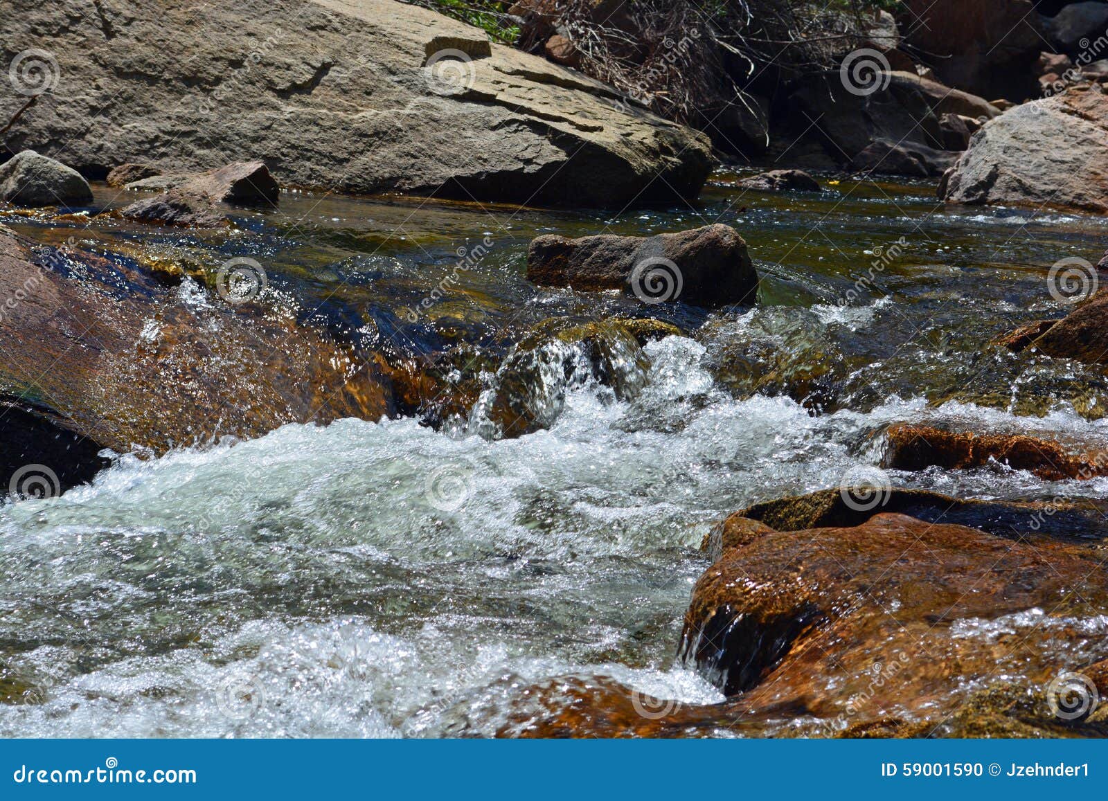 Stream Water Flows By Big Rocks. Water flows over rocks with big boulders in the background.