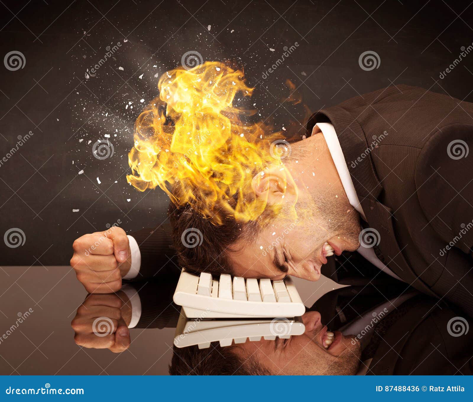 Stressed business man`s head is burning. A depressed businessman banging his head in a keyboard and shouting with his head on fire, reflecting on desk