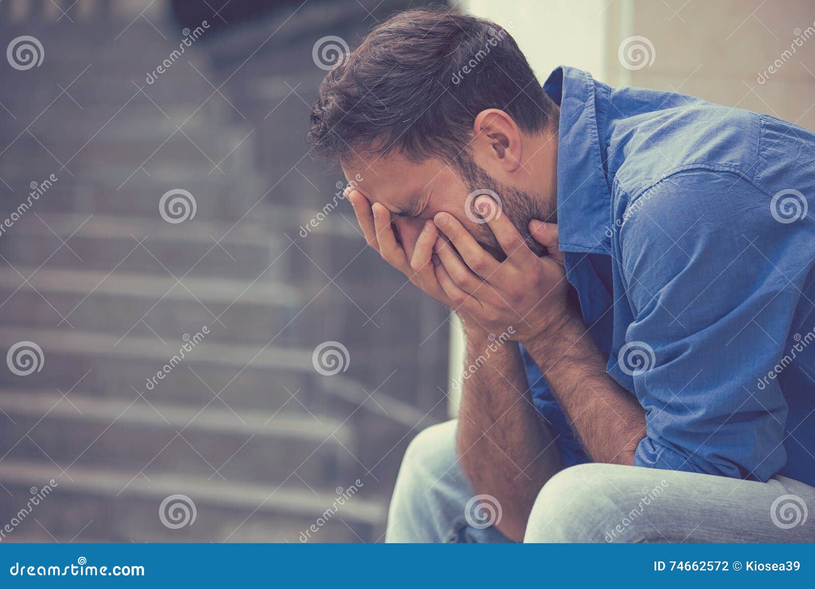 stressed sad crying man sitting outside holding head with hands