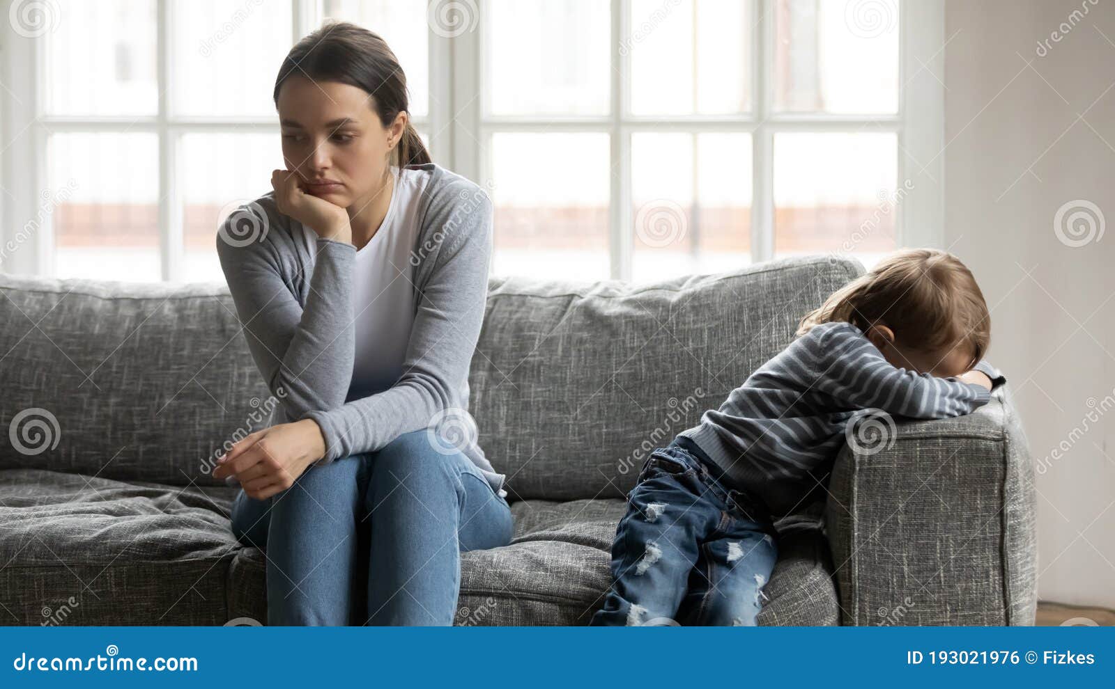 stressed young mommy sitting separate on couch with offended son.