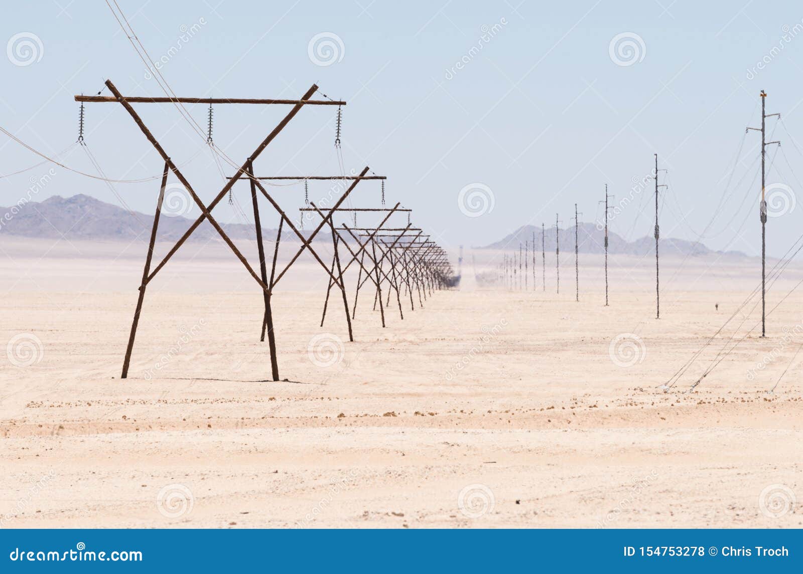 Stromleitungen und Telefonleitungen verzerrt durch die Hitze in der Namibia-Wüste. Alte hölzerne Pfostenstrukturen, die Strom durch die Namibia-Wüste in der brennenden Hitze übertragen, insoweit das Auge sehen kann