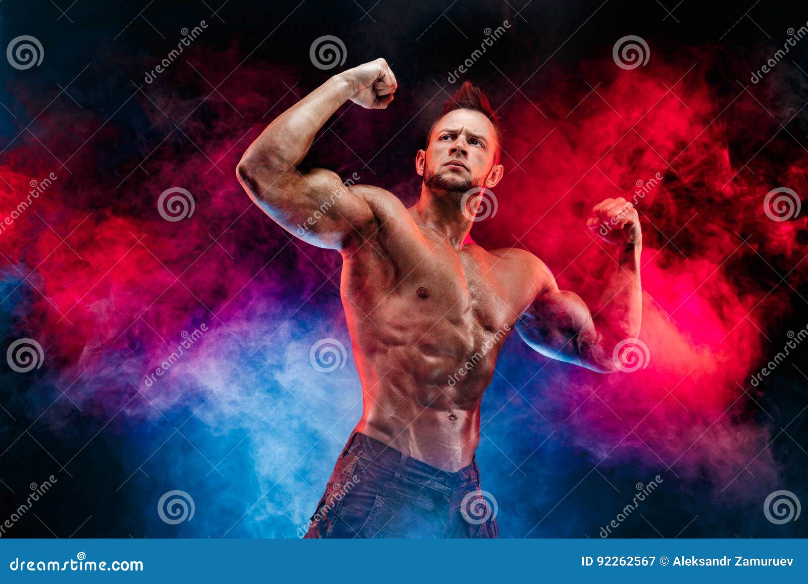 Strong bodybuilder with six pack, perfect abs, shoulders, biceps, triceps  and chest, personal fitness trainer flexing his muscles in smoke Stock  Photo