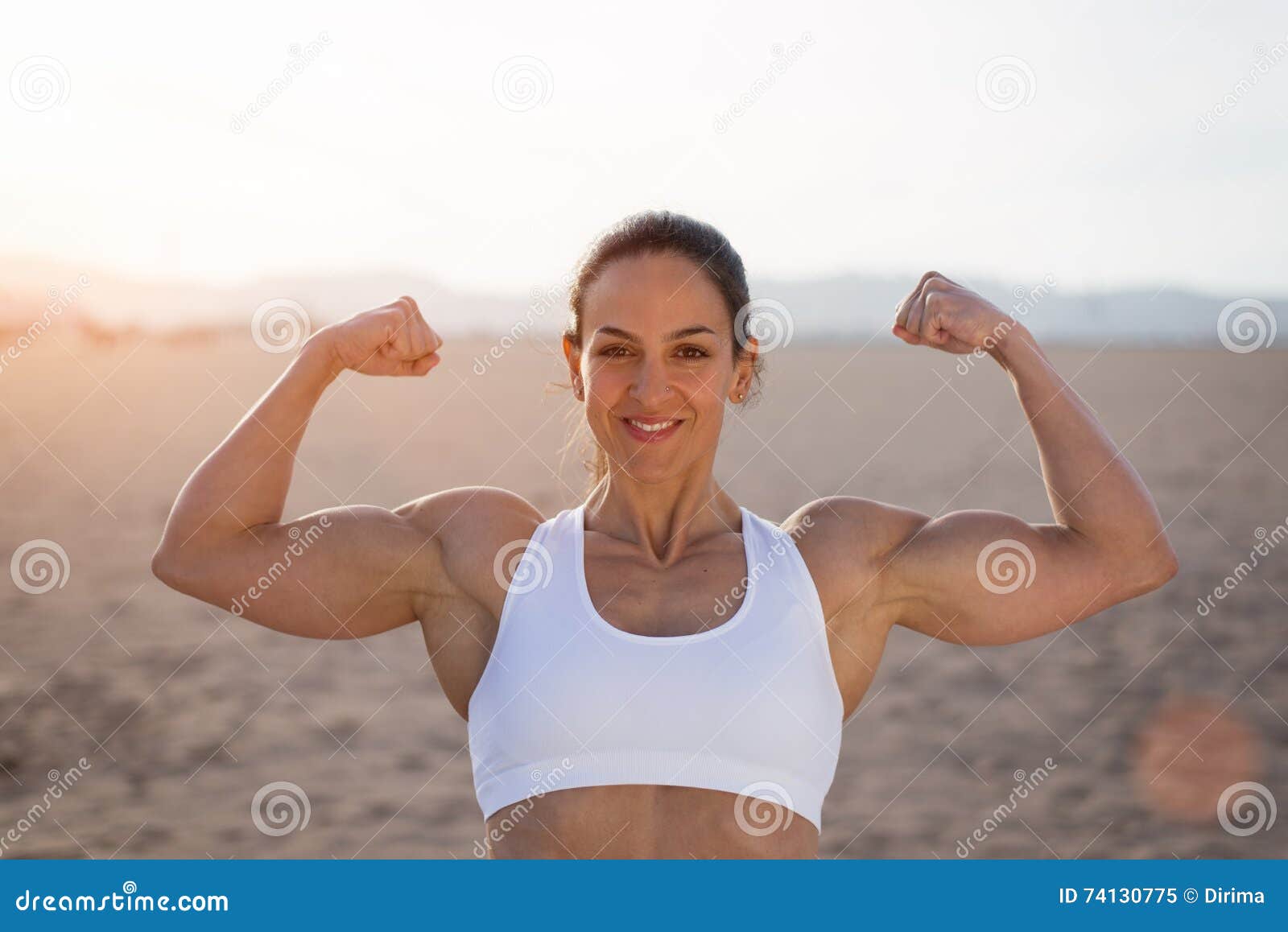 Fitness woman showing fit strong arms triceps and shoulder. Female  bodybuilder athlete flexing muscles after outdoor workout at the beach.  Stock Photo