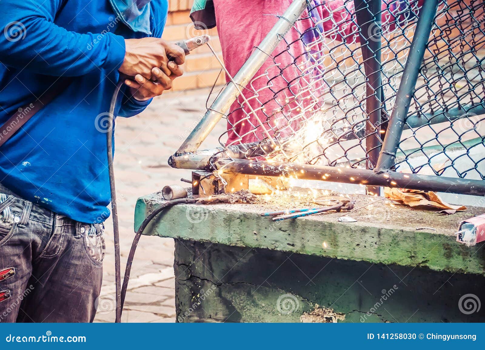 a strong man is a welder in a blue t-shirt,and welders leathers, a metal product is welded with a welding machine in the outdoor