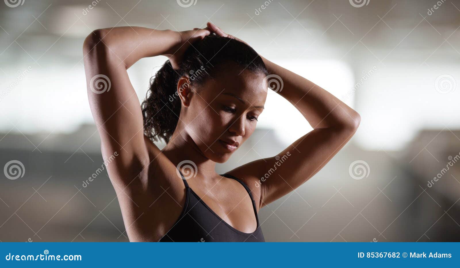 Strong Millennial Woman Standing with Arms Over Head Stock Photo