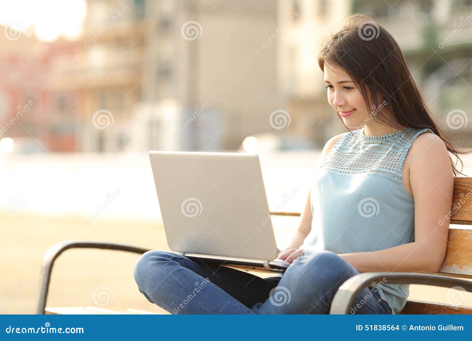 student girl browsing a laptop sitting in a bench