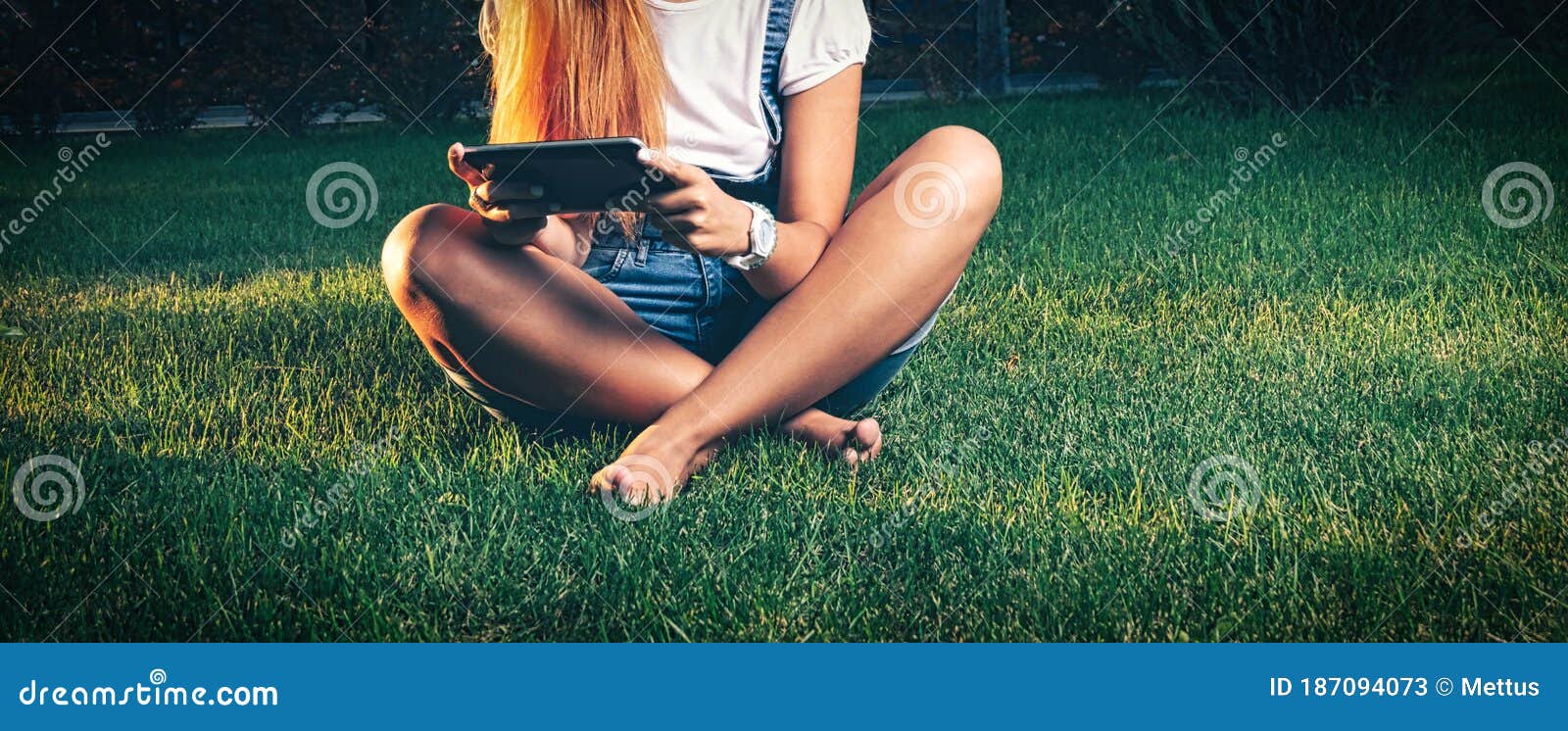 studente in park e-learning on tablet pc sitting cross-legged on the grass