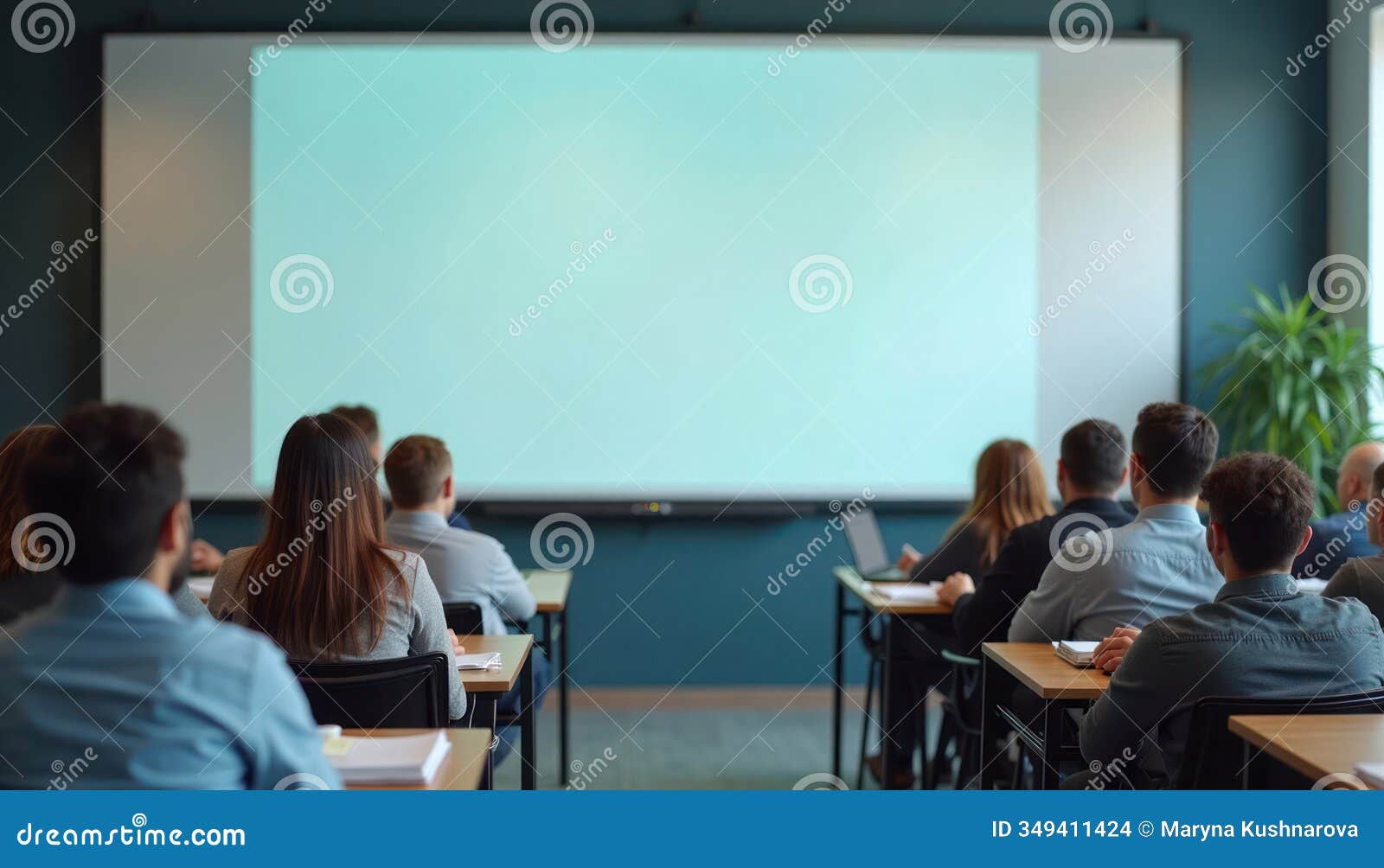 students attend class session in modern hybrid classroom. students in person at desks others attend remotely on large screen.