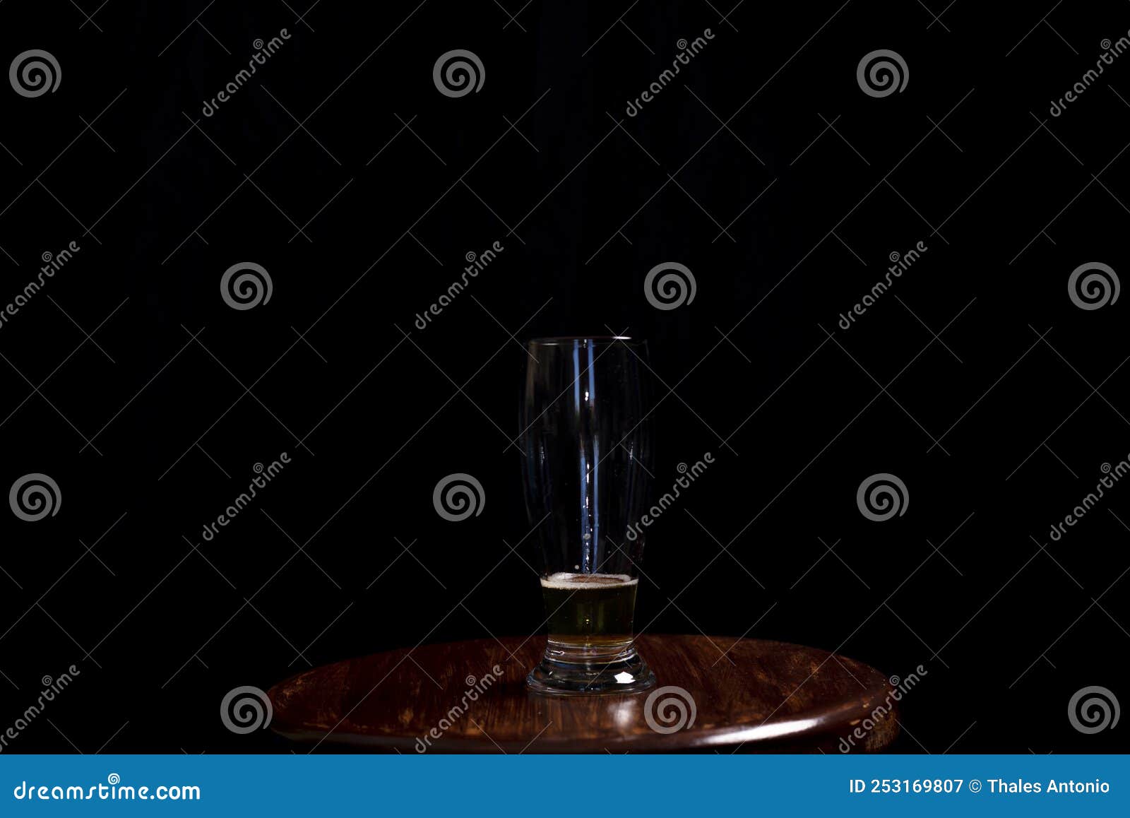 studio portrait of a glass cup with yellow liquid, on top of a wooden bench, against a black studio background