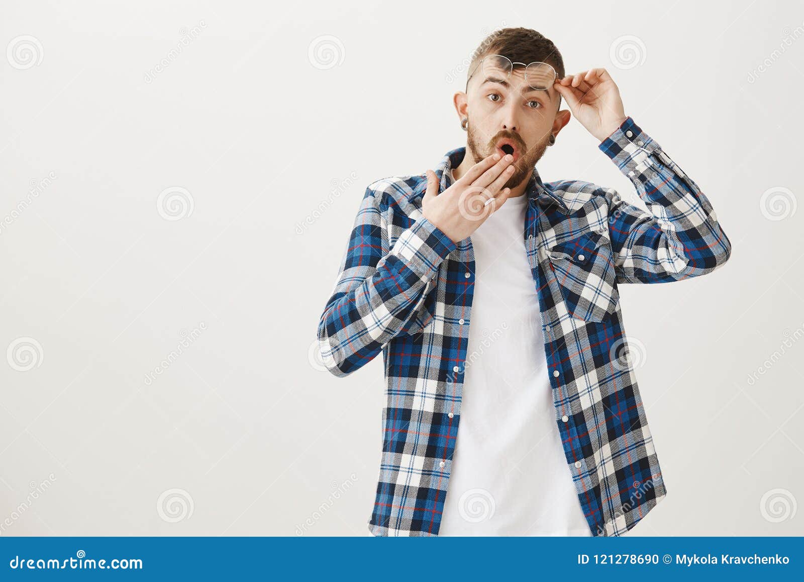 studio portrait of shocked worried attractive man with beard, taking off glasses and holding eyewear near forehead