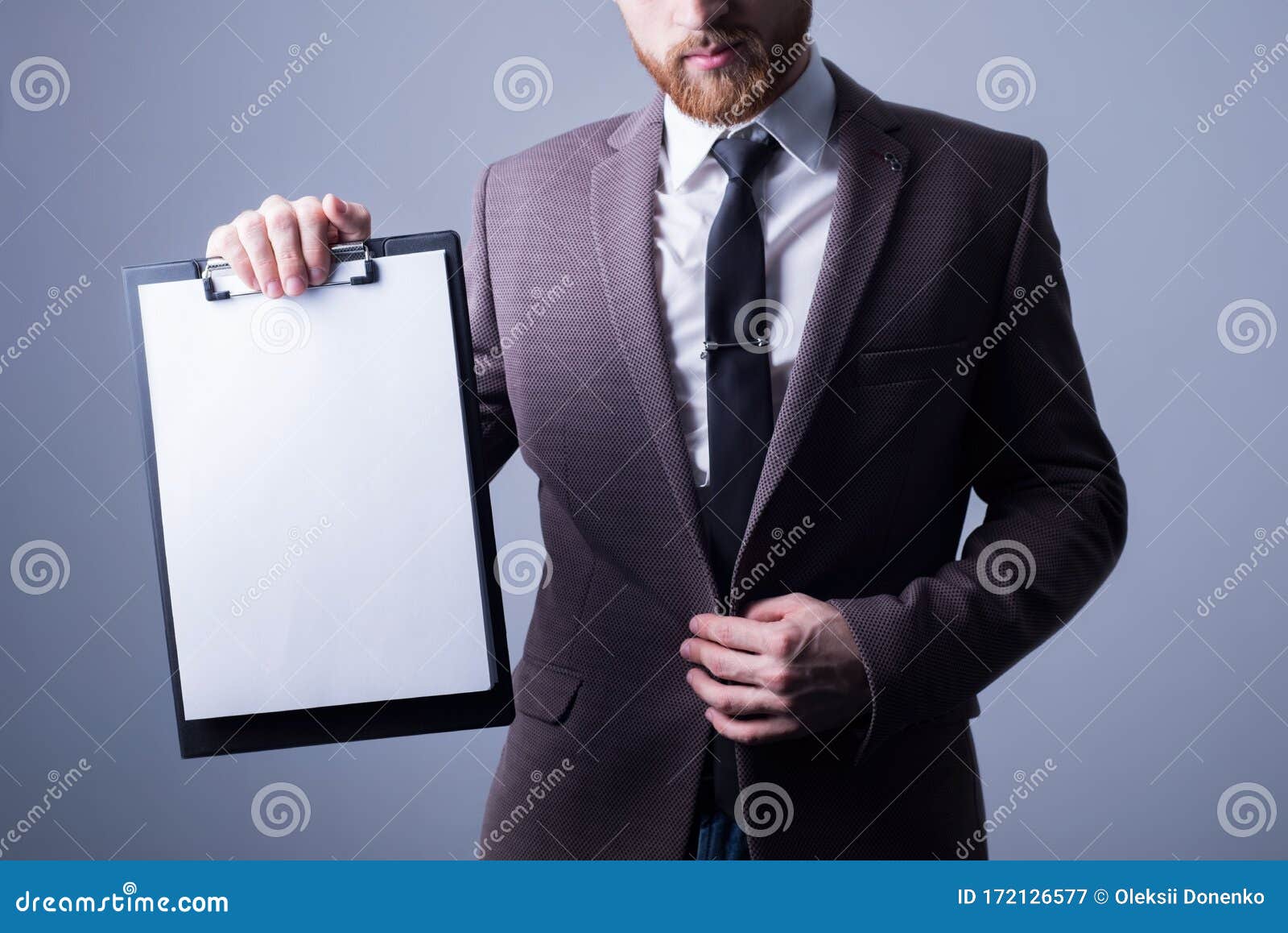 studio portrait of a young bearded handsome guy of twenty-five, in an official suit, holding a folder with a reading sheet for