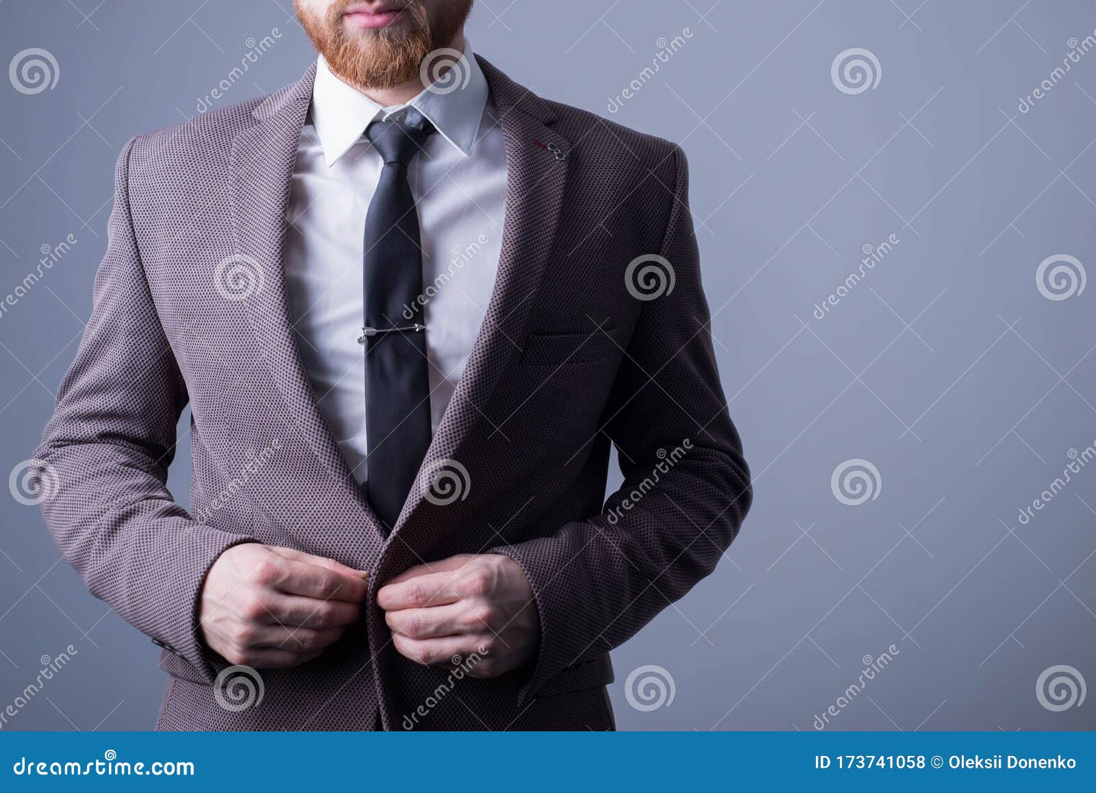 studio portrait of a young bearded handsome guy of twenty-five years old, in an official suit, buttoning a button in a jacket. on