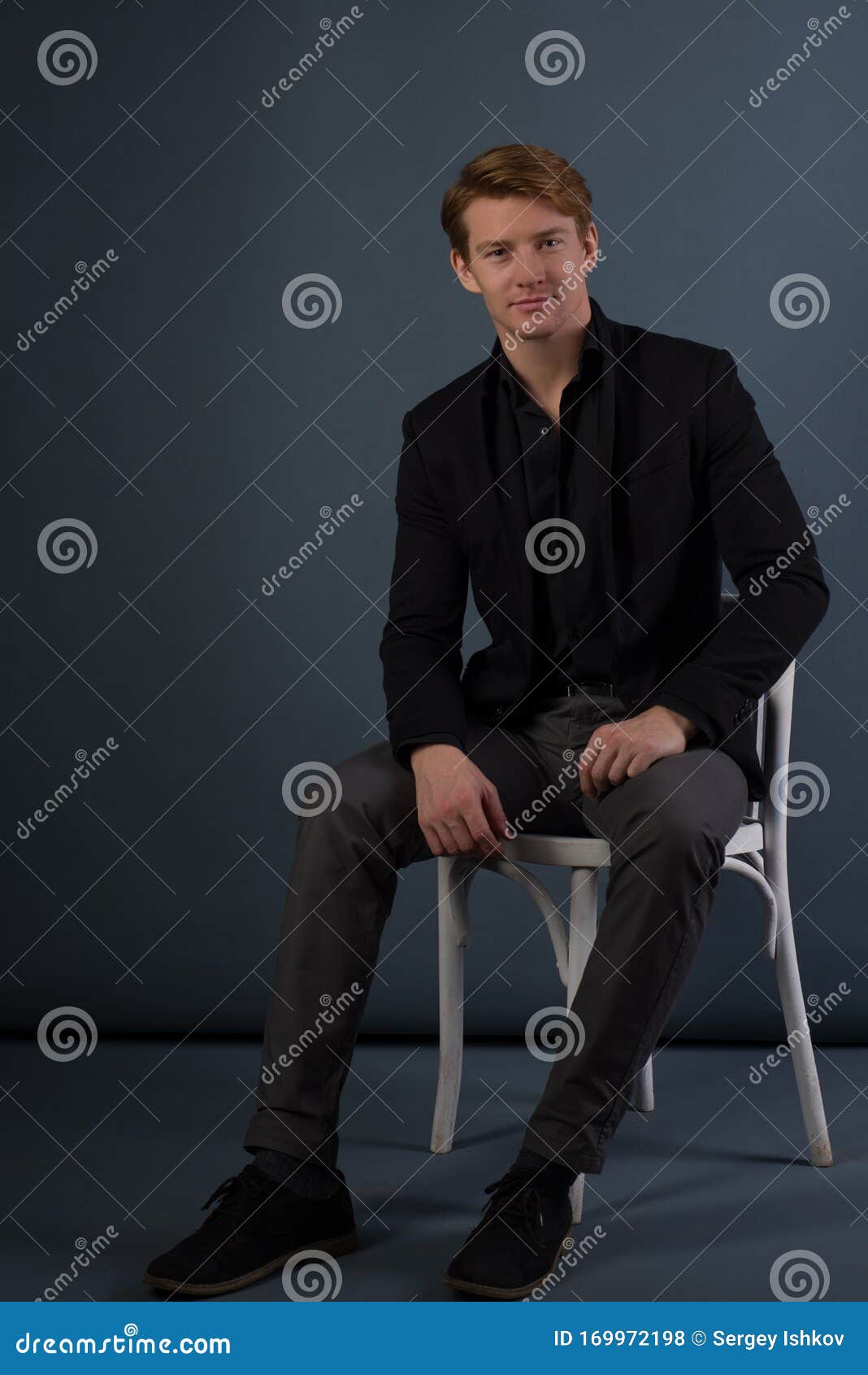 Studio Shot Of Handsome Young Man Sitting On The Chair And Looking At ...