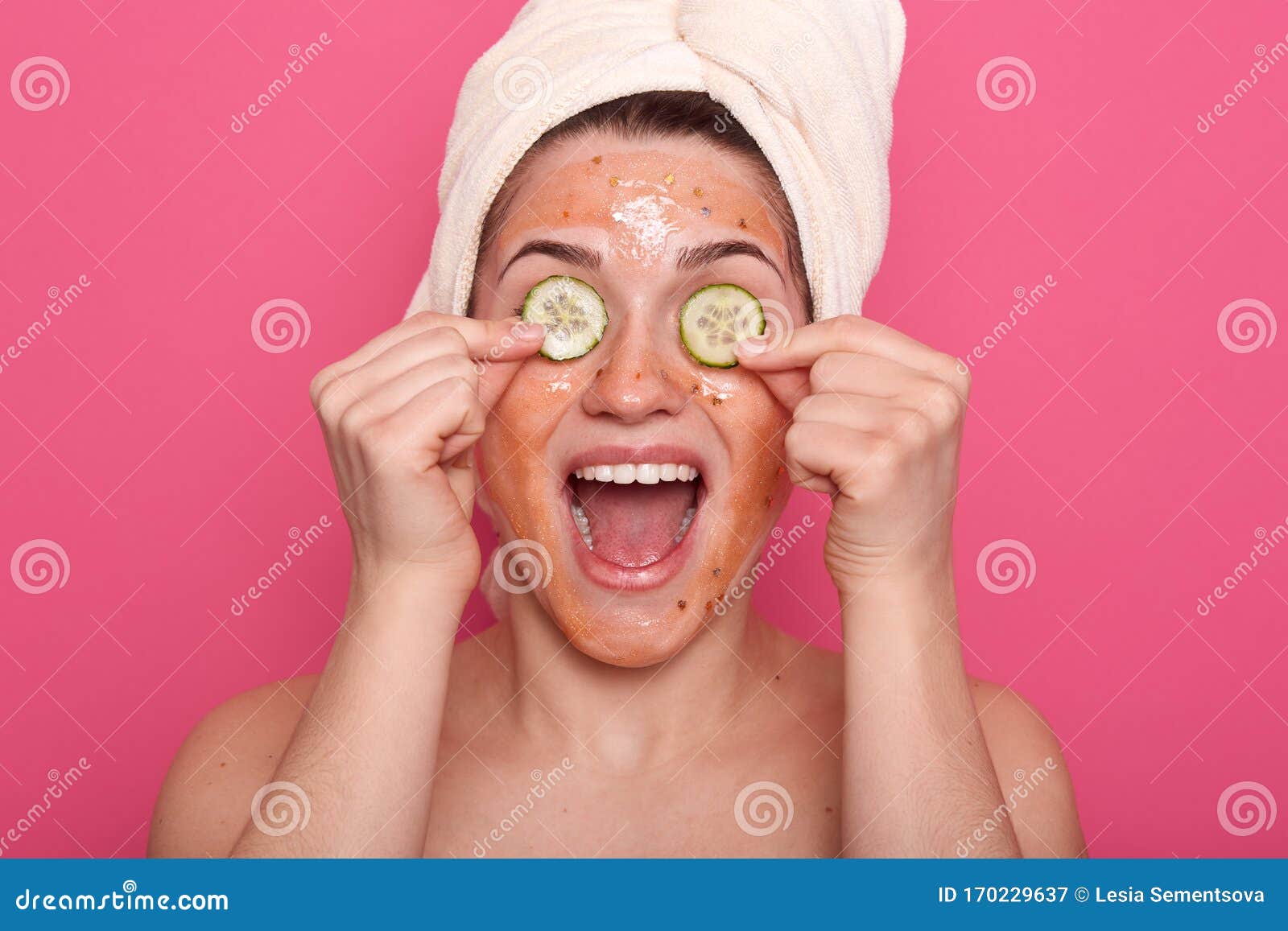 studio shot of satisfaited woman applies slices of cucumber on her eyes and having scrabmask on face, has happy expresion, opens