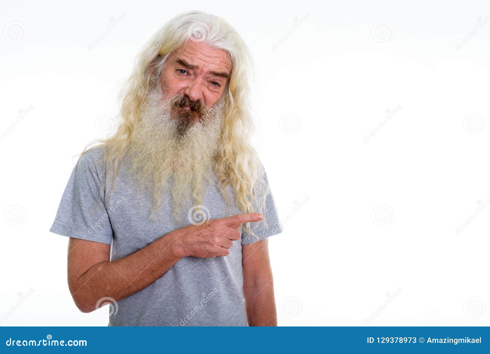 Studio shot of senior bearded man looking disgusted while pointing to the side