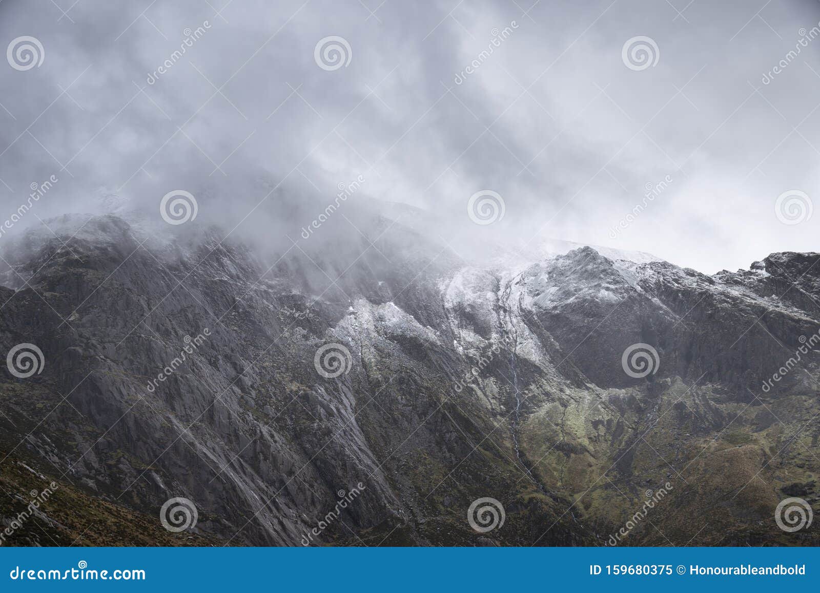 stunning dramatic landscape image of snowcapped glyders mountain range in snowdonia during winter with menacing low clouds hanging