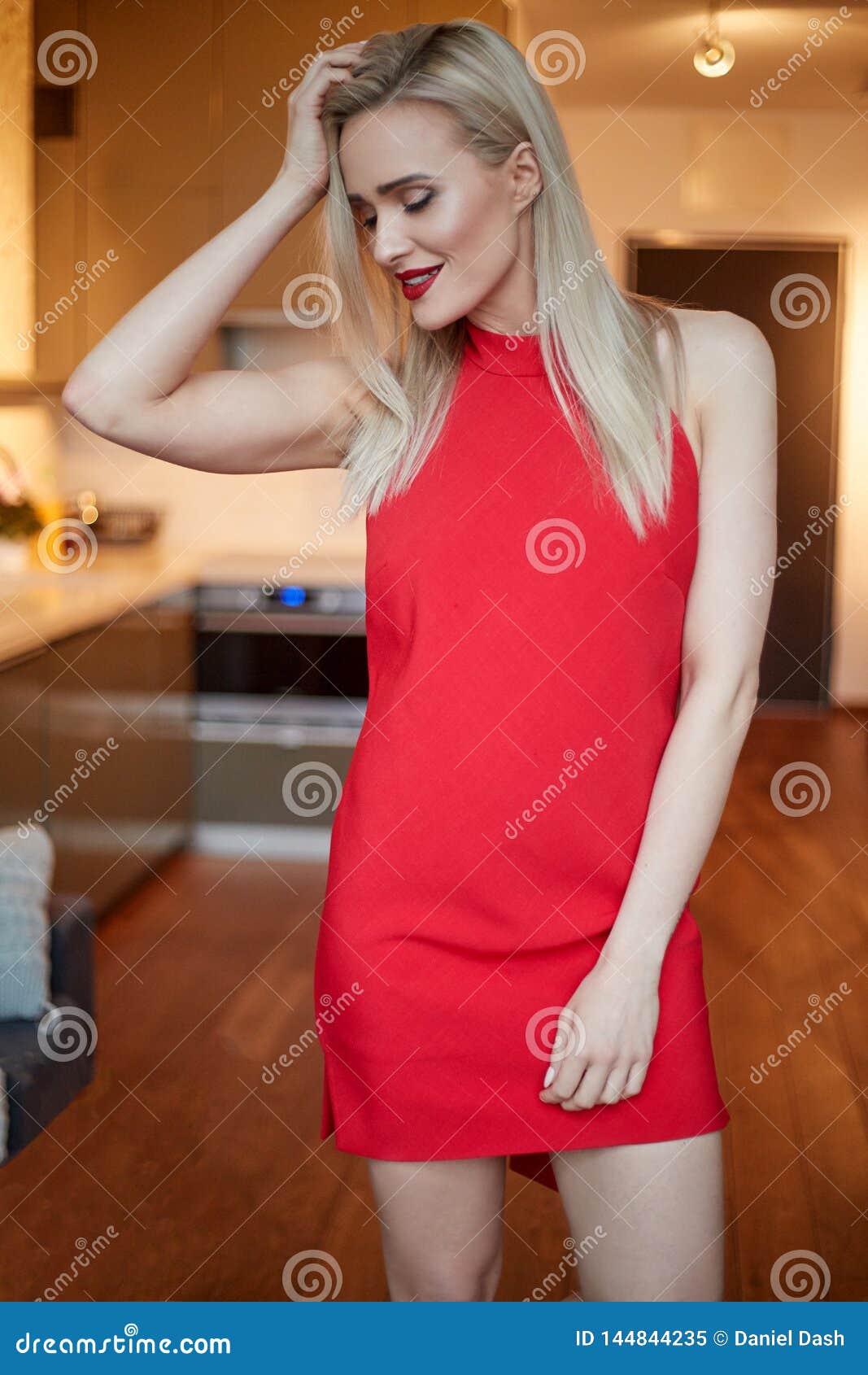 Stylish Elegant Blonde Woman in Home Living Room, Wearing Red Dress