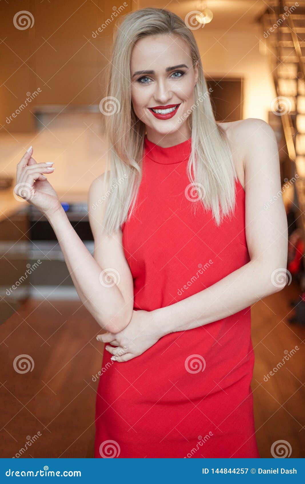 Stylish Elegant Blonde Woman in Home Living Room, Wearing Red Dress