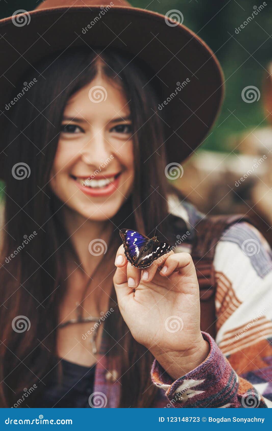 stylish hipster,happy woman in hat holding apatura iris on fingers in forest in mountains. beautiful butterfly on girl hand.