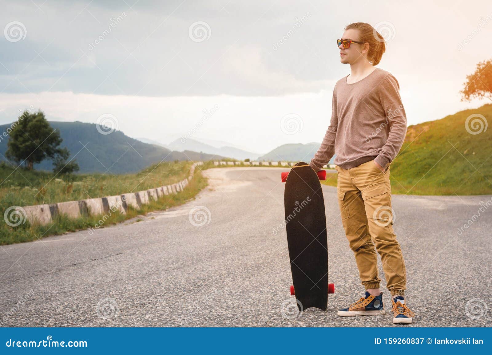 Stylish Young Man Standing Along a Winding Mountain Road with a Skate ...