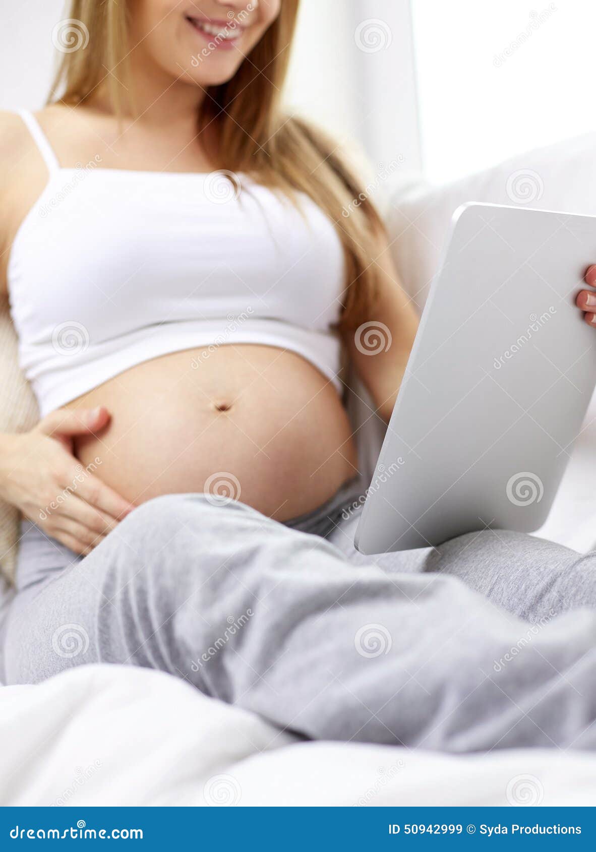 Stäng sig upp av gravid kvinna med minnestavlaPC hemma. Havandeskap, moderskap, teknologi, folk och förväntanbegrepp - som är nära upp av lycklig gravid kvinna med minnestavlaPCdatoren hemma