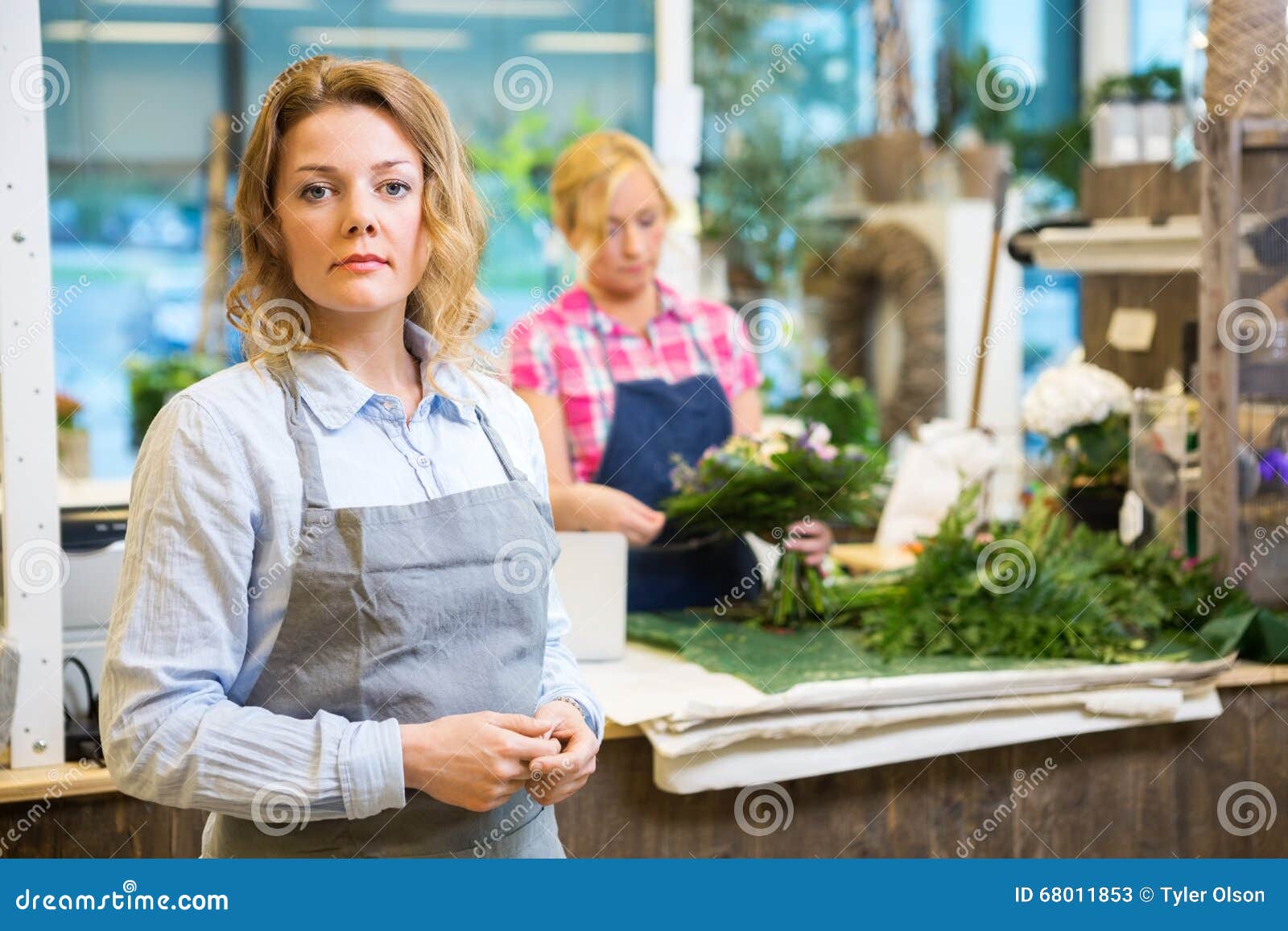 Stående av den säkra kvinnliga blomsterhandlaren In Shop. Stående av den säkra kvinnliga blomsterhandlaren med kollegadanandebuketten i bakgrund