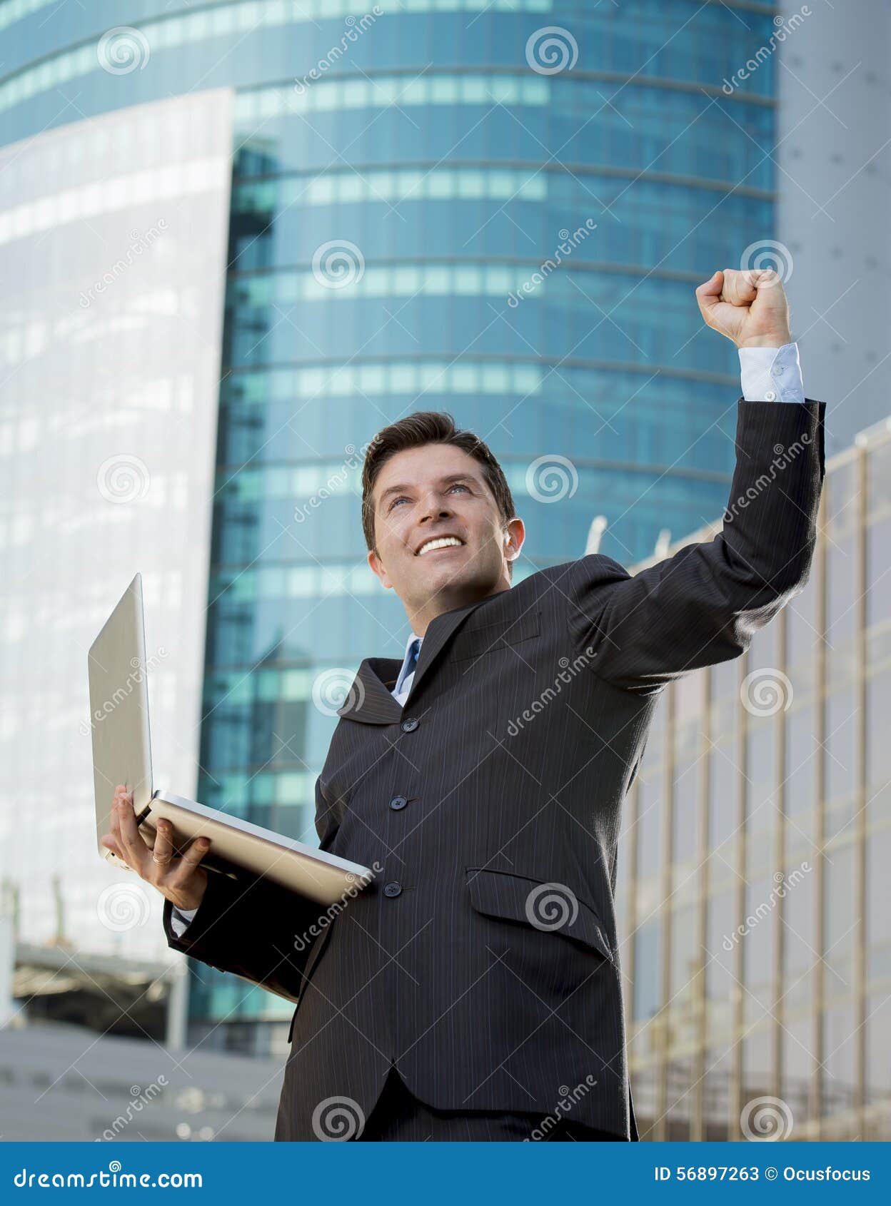 Successful businessman with computer laptop happy doing victory sign. Young attractive and successful businessman in suit and tie with computer laptop happy and excited doing victory sign after reaching business goal outdoors at urban city financial district