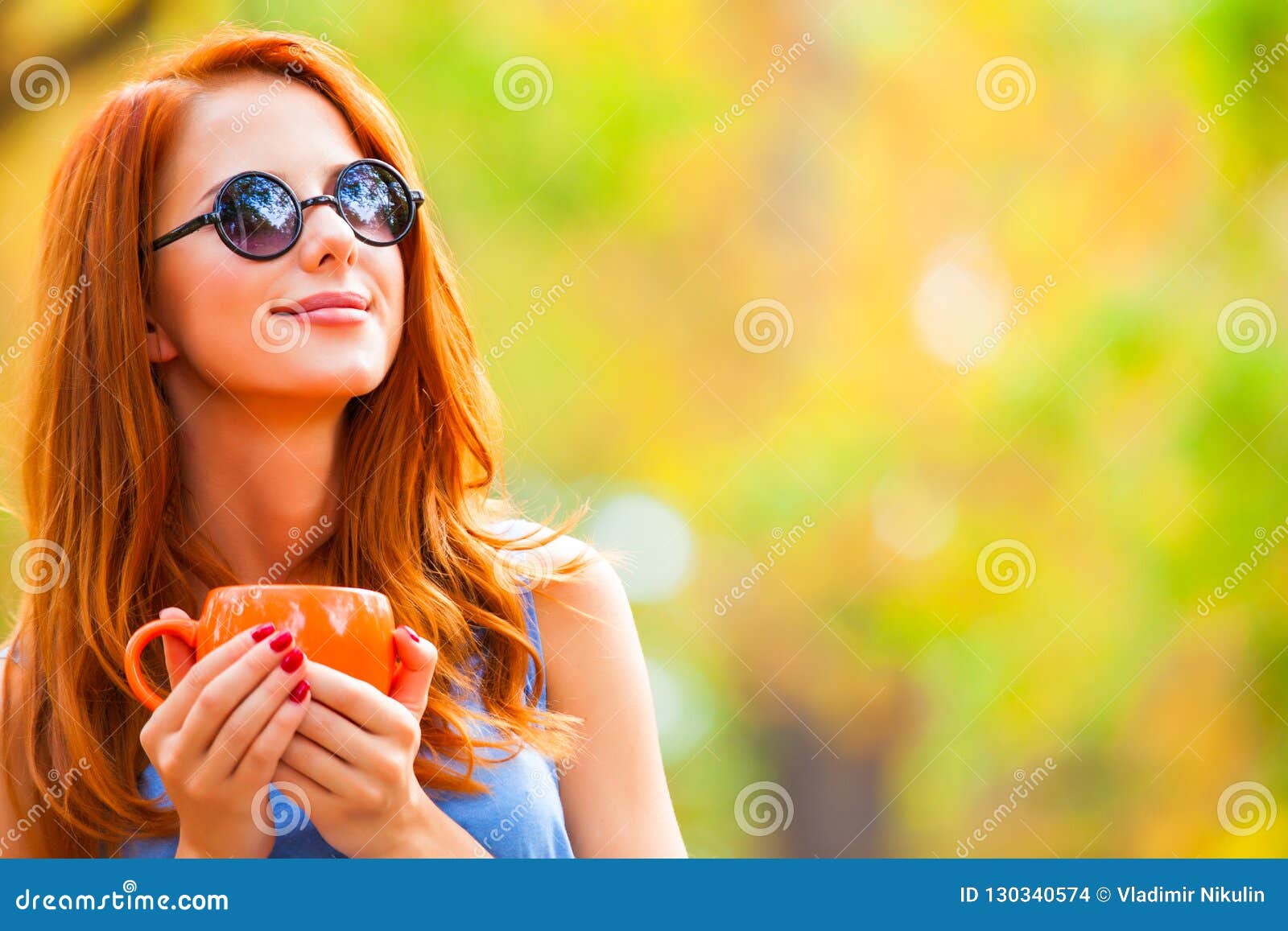 successful redhead girl winh cup in the autumn park.