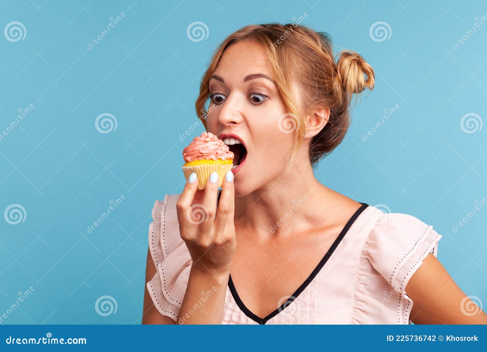 sugar addiction. portrait of hungry blonde young adult woman in dress biting delicious cake, looking with desire to eat sweet